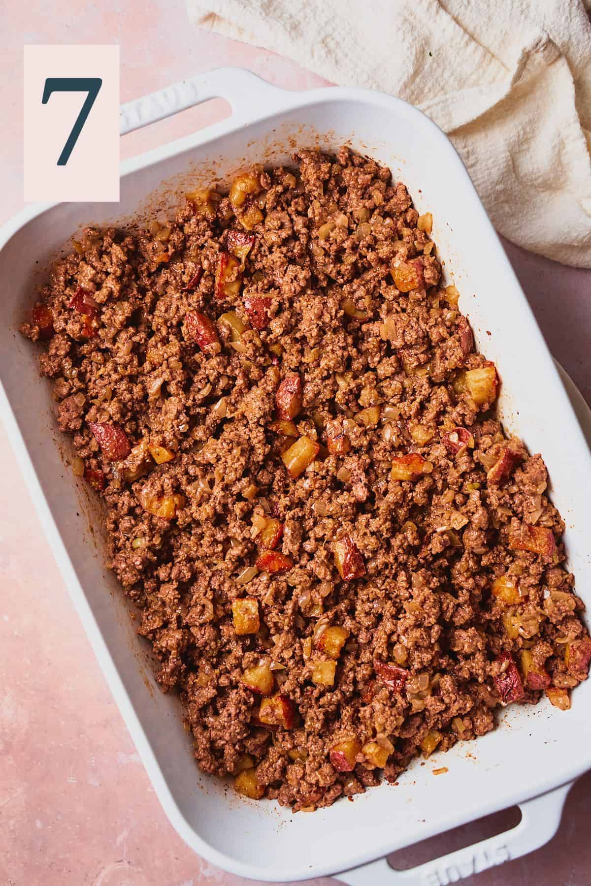 Ground beef and cooked potatoes in a white casserole dish. 