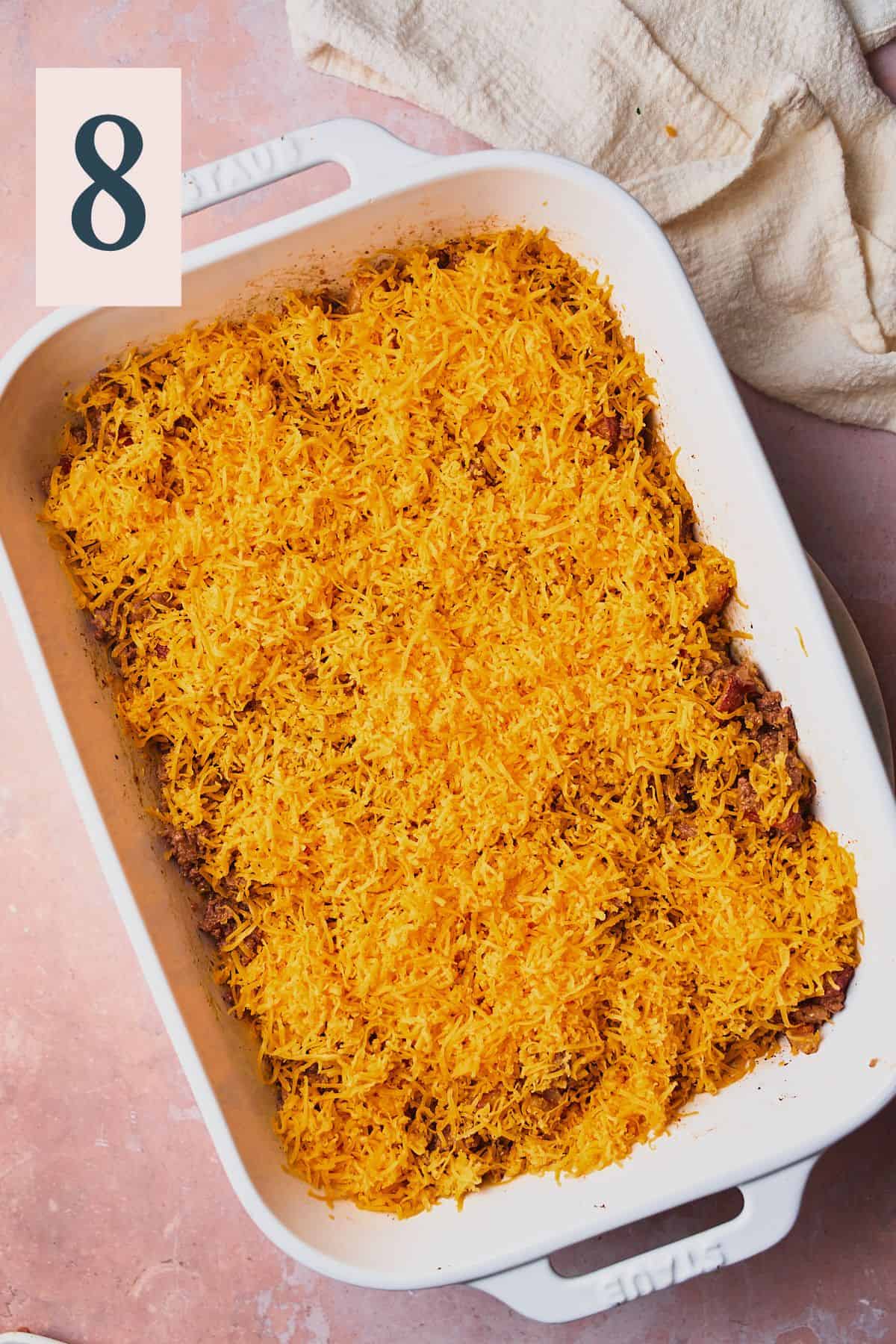 Shredded cheese covering beef and potatoes in a casserole dish. 