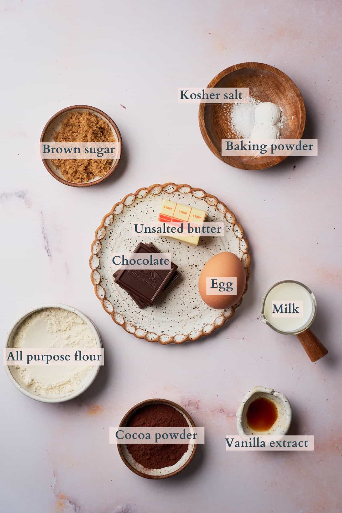 Ingredients to make chocolate lava mug cake on a table laid out and labeled to denote each ingredient.