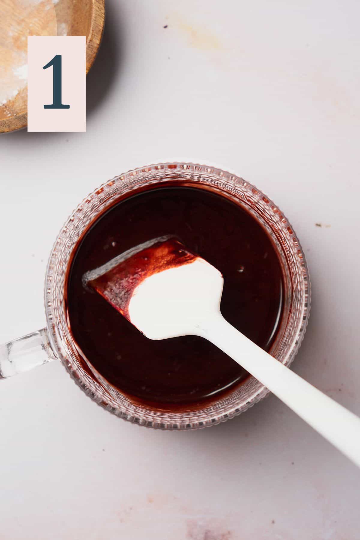 Melted butter with cocoa powder in a large mug with a rubber spatula stirring it. 