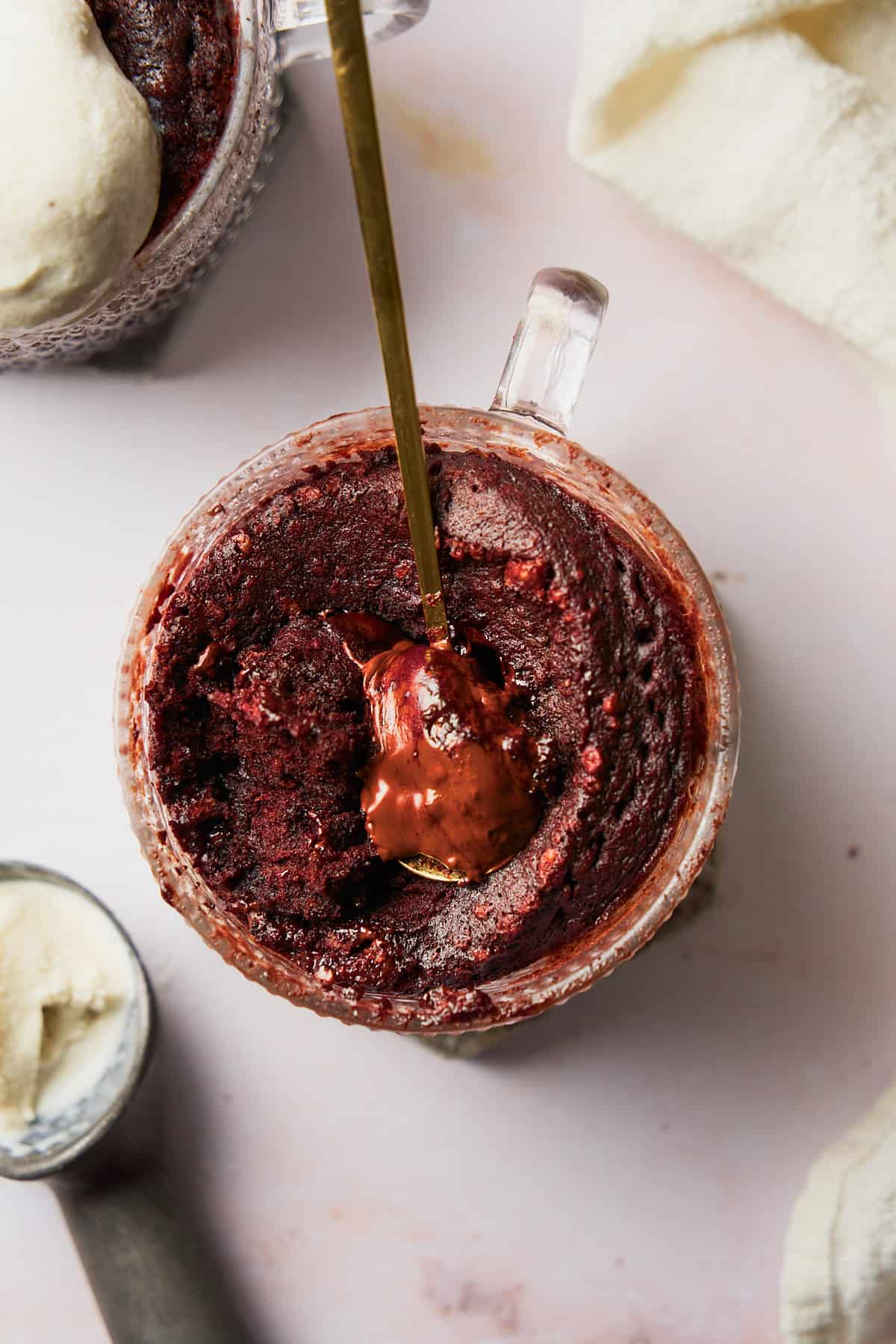 Close up shot of a chocolate lava mug cake with a spoon showing the melted chocolate interior, with ince cream on the side. 