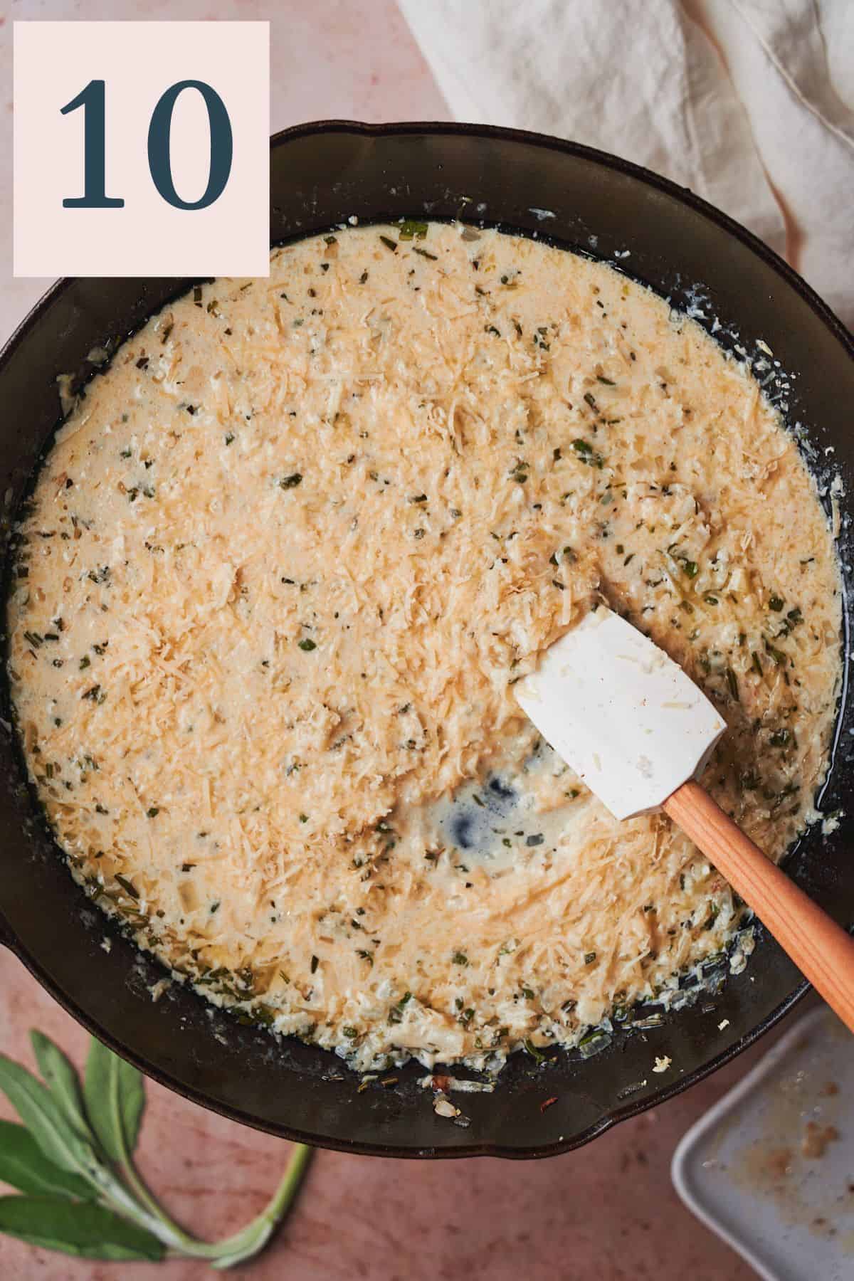 Thickened creamy sauce with cheese, onions, garlic, and herbs in a skillet with a rubber spatula. 