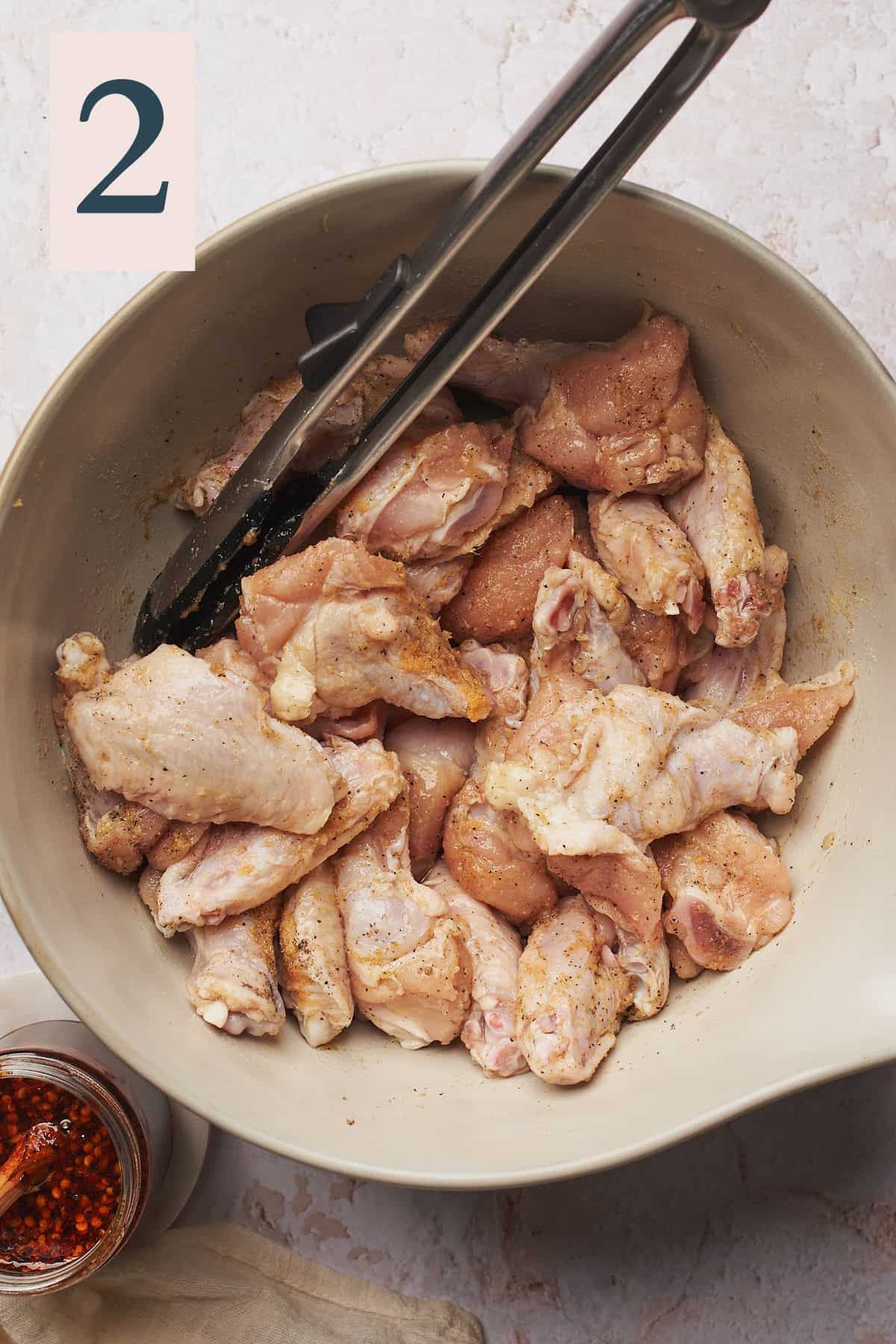 raw chicken wings seasoned in a bowl with tongs.
