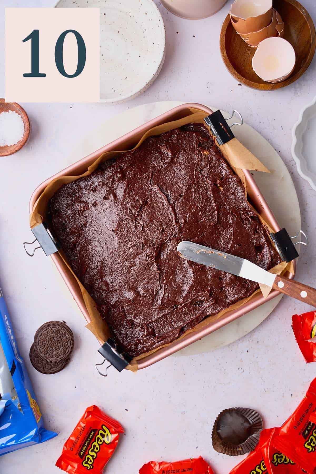 Spreading brownie batter over the top of mix-ins in a square baking pan. 