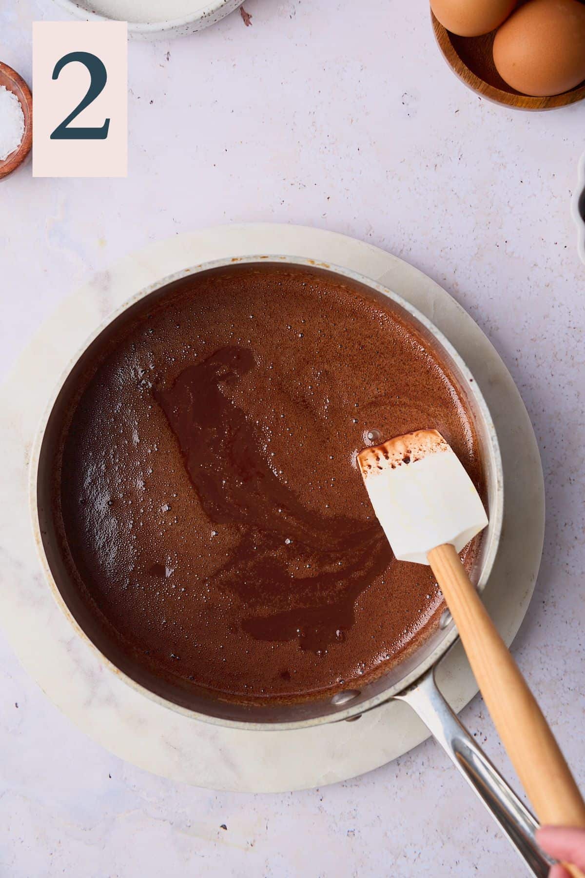 Melted chocolate and butter mixture in a saucepan with a rubber spatula. 