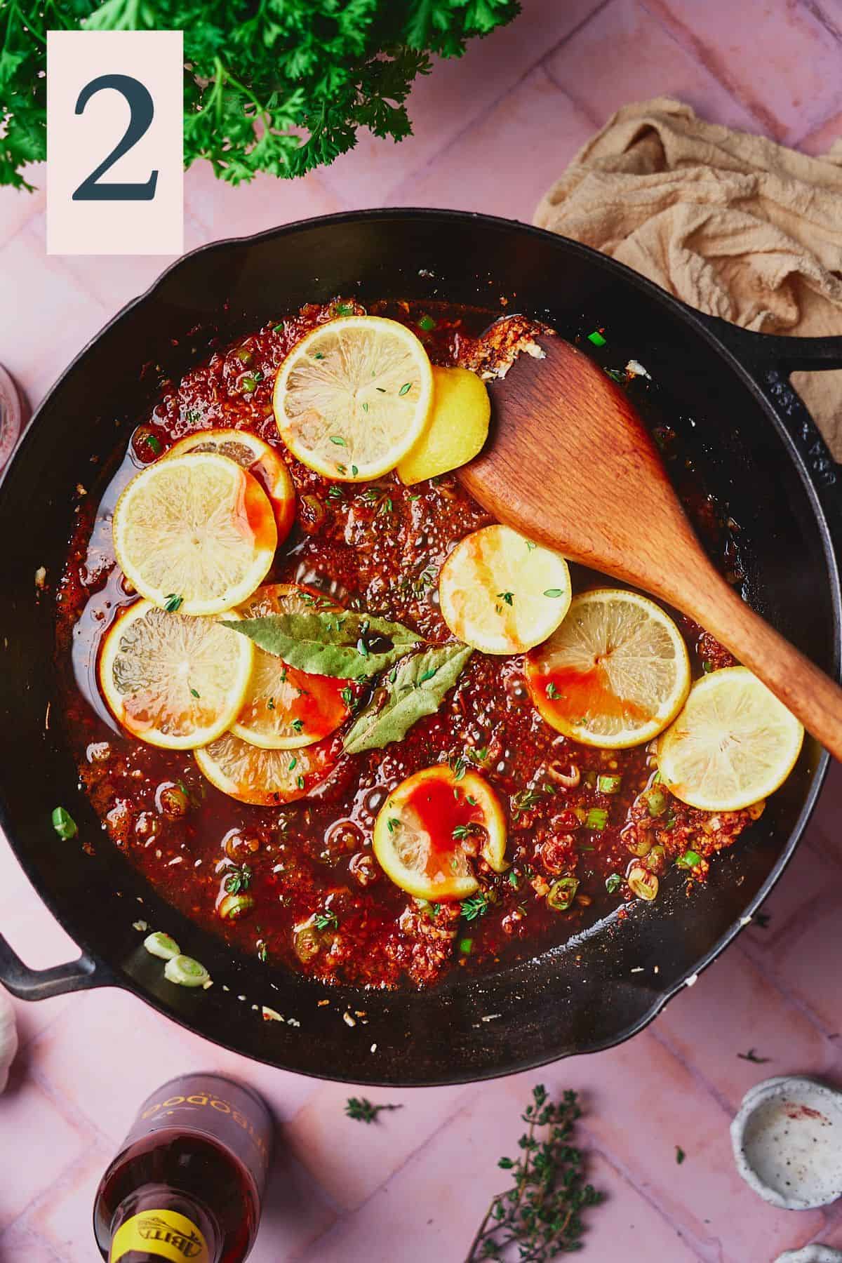 Sauce with spices, lemons, hot sauce, bay leaves, beer, garlic, and green onions in a skillet. 