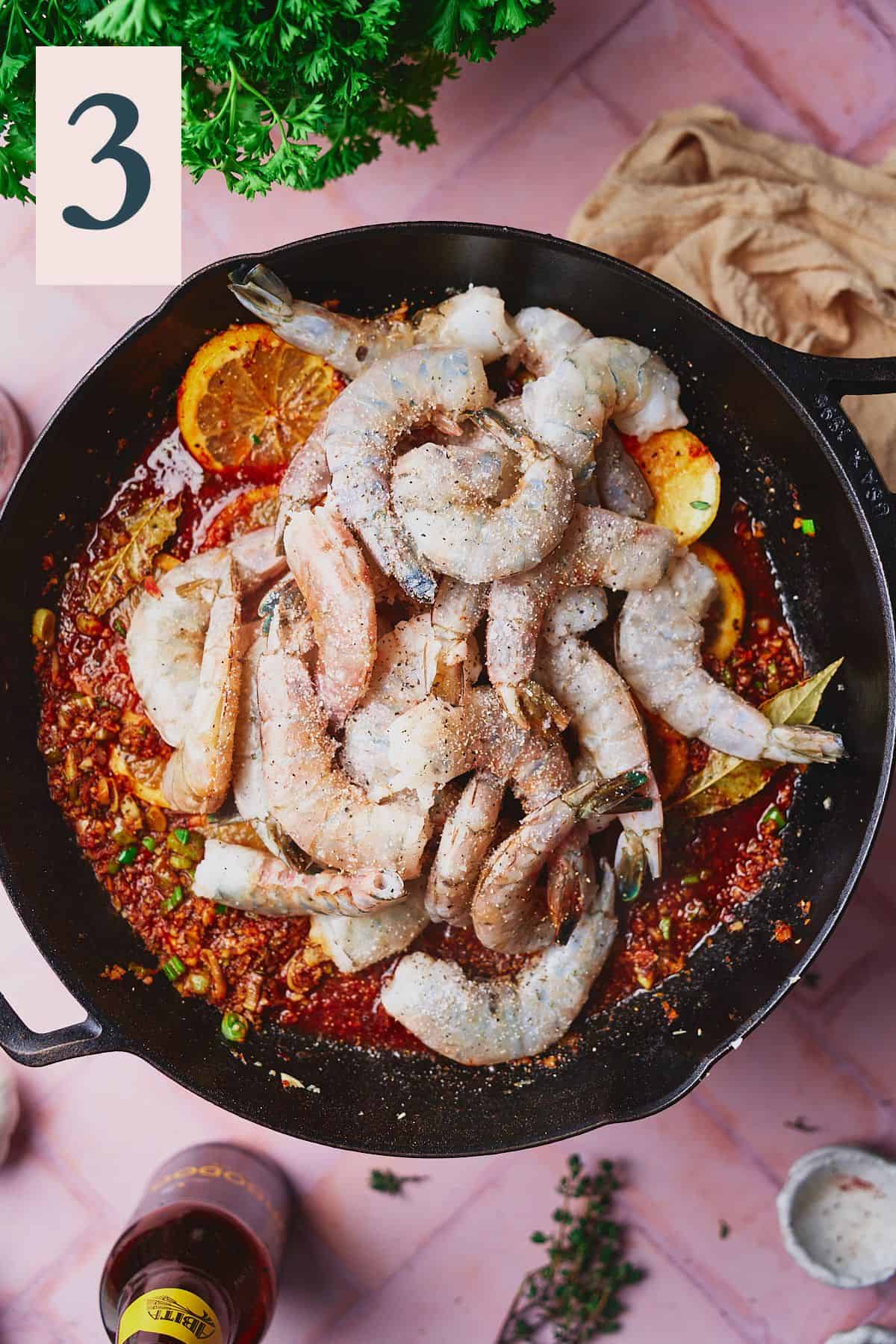 Shrimp added to a skillet with a bright red lemony sauce, and seasoned with salt and pepper. 