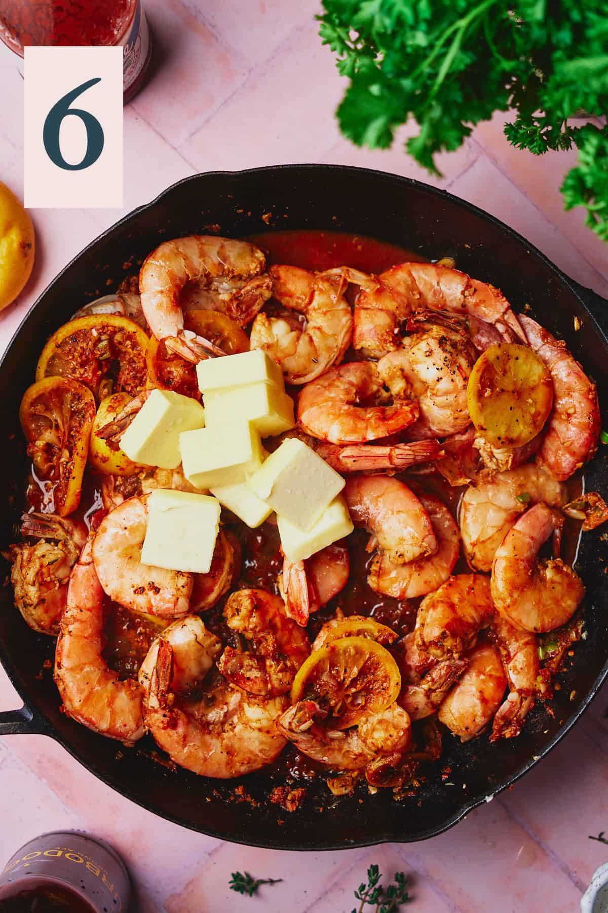 Cooked shrimp in a skillet with cubed butter added. 