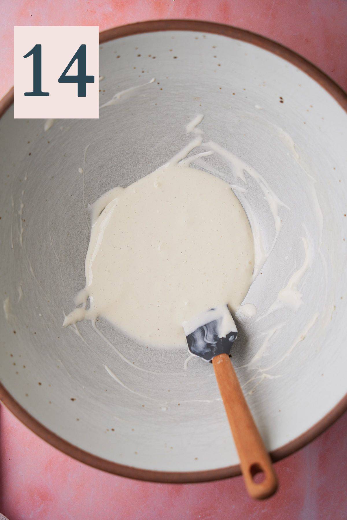 Thin cream cheese icing in a bowl with a rubber spatula. 