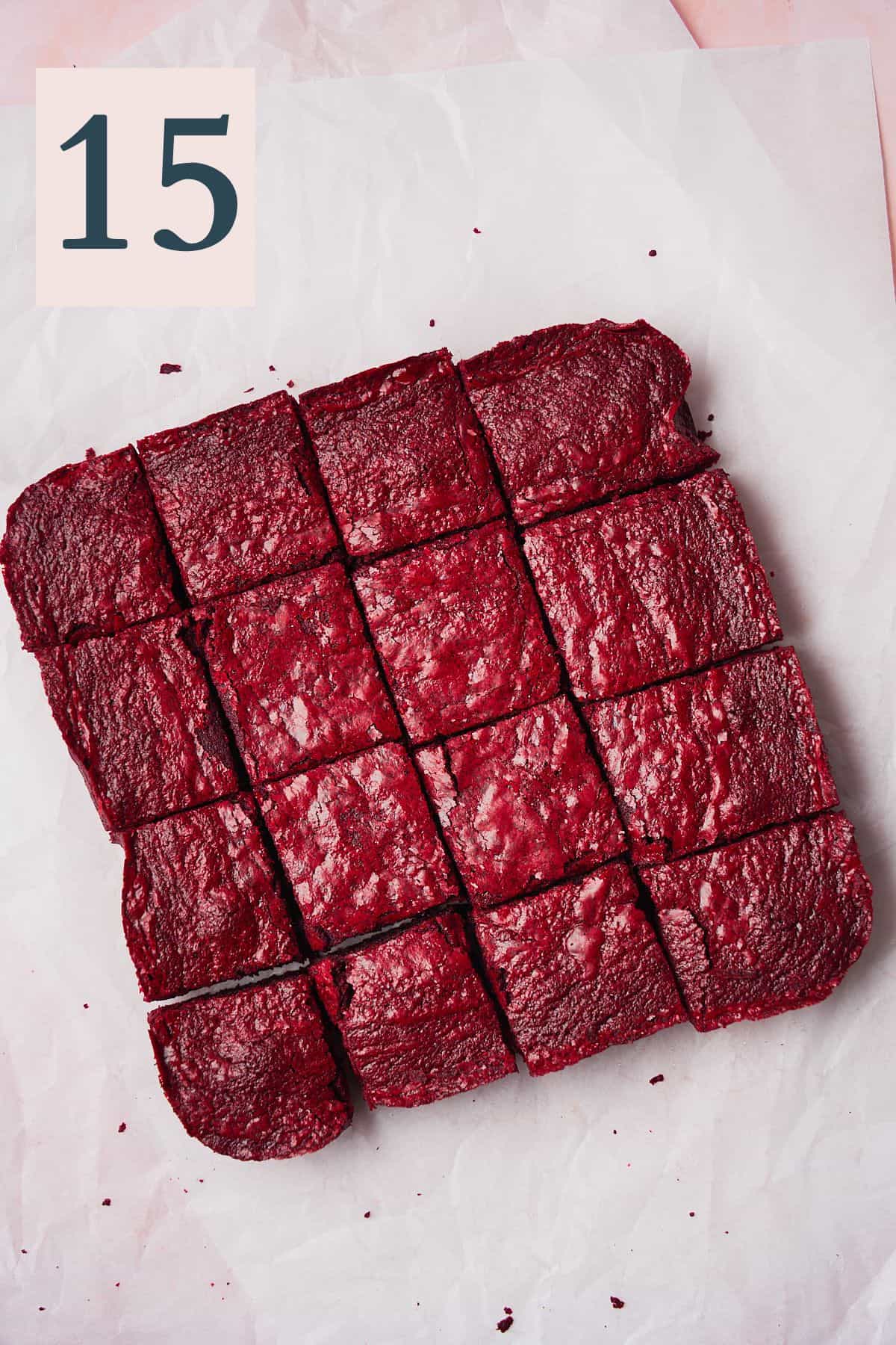Red velvet brownies cut into 16 square pieces on crinkled white parchment paper. 