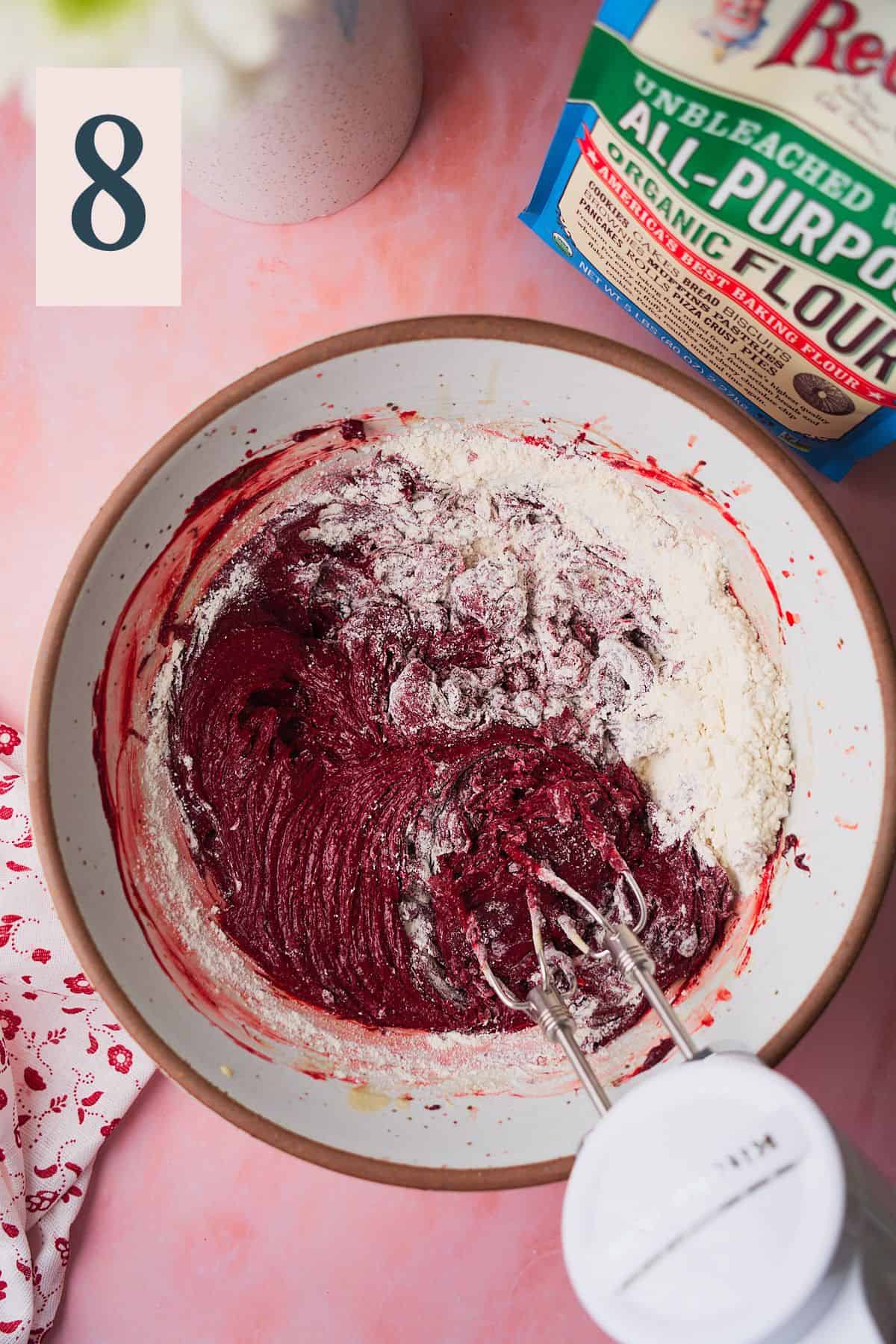Mixing red velvet brownies with flour added in a large bowl with an electric mixer. 