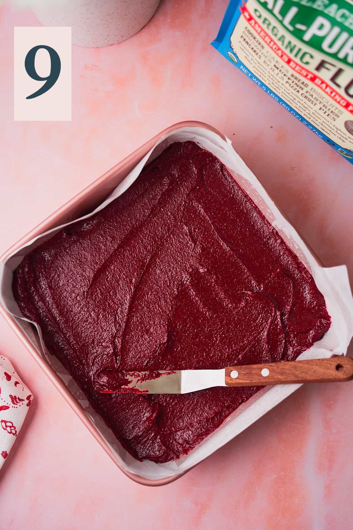 Red velvet brownies being smoothed in a baking pan with an offset spatula. 