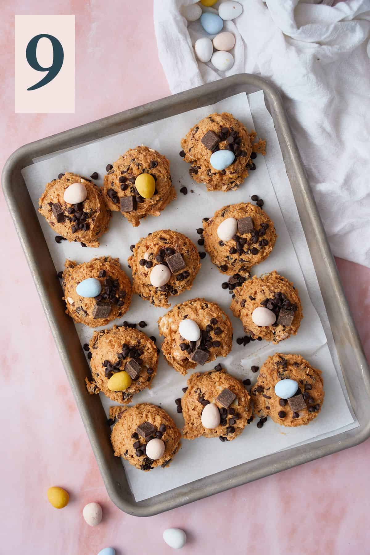 Large scooped cookie dough balls on a parchment lined baking sheet and topped with Cadbury eggs. 