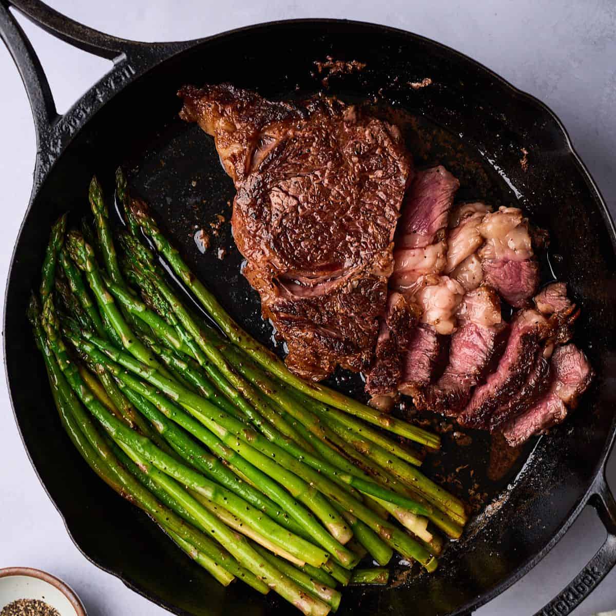 Ribeye steak and asparagus cooked in a cast iron skillet and cut into to reveal the center cooked a perfect medium rare.