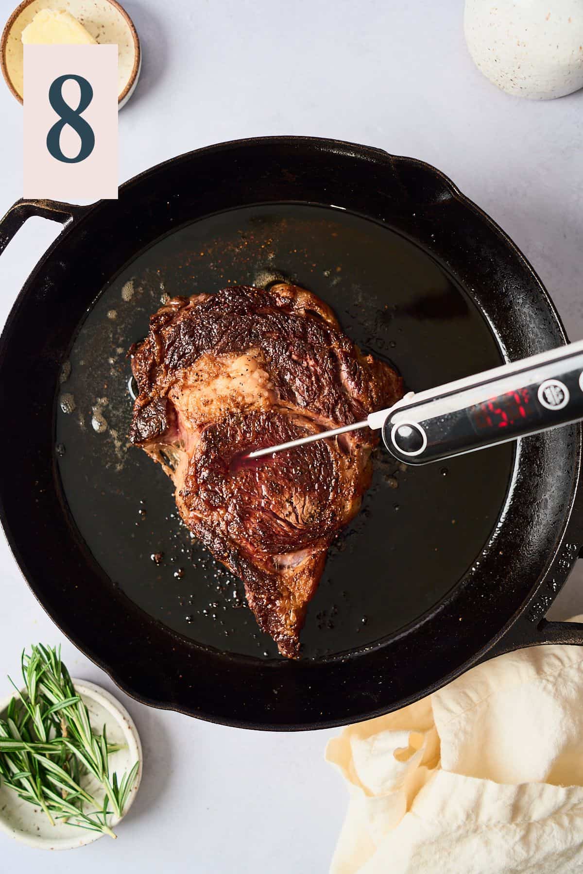 Ribeye steak in a cast iron skillet with a digital thermometer in it that reads 115.7°F. 