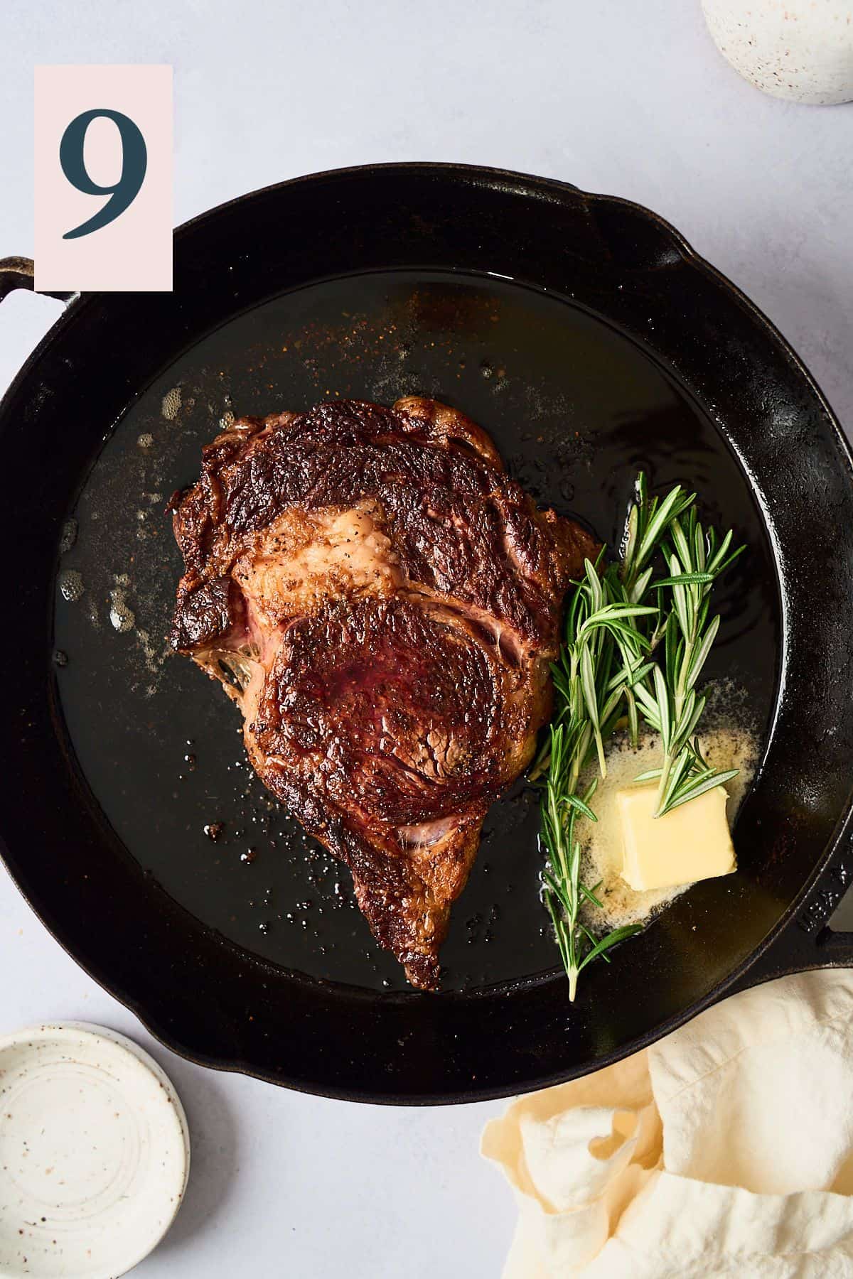 Steak in a skillet with butter and rosemary added. 