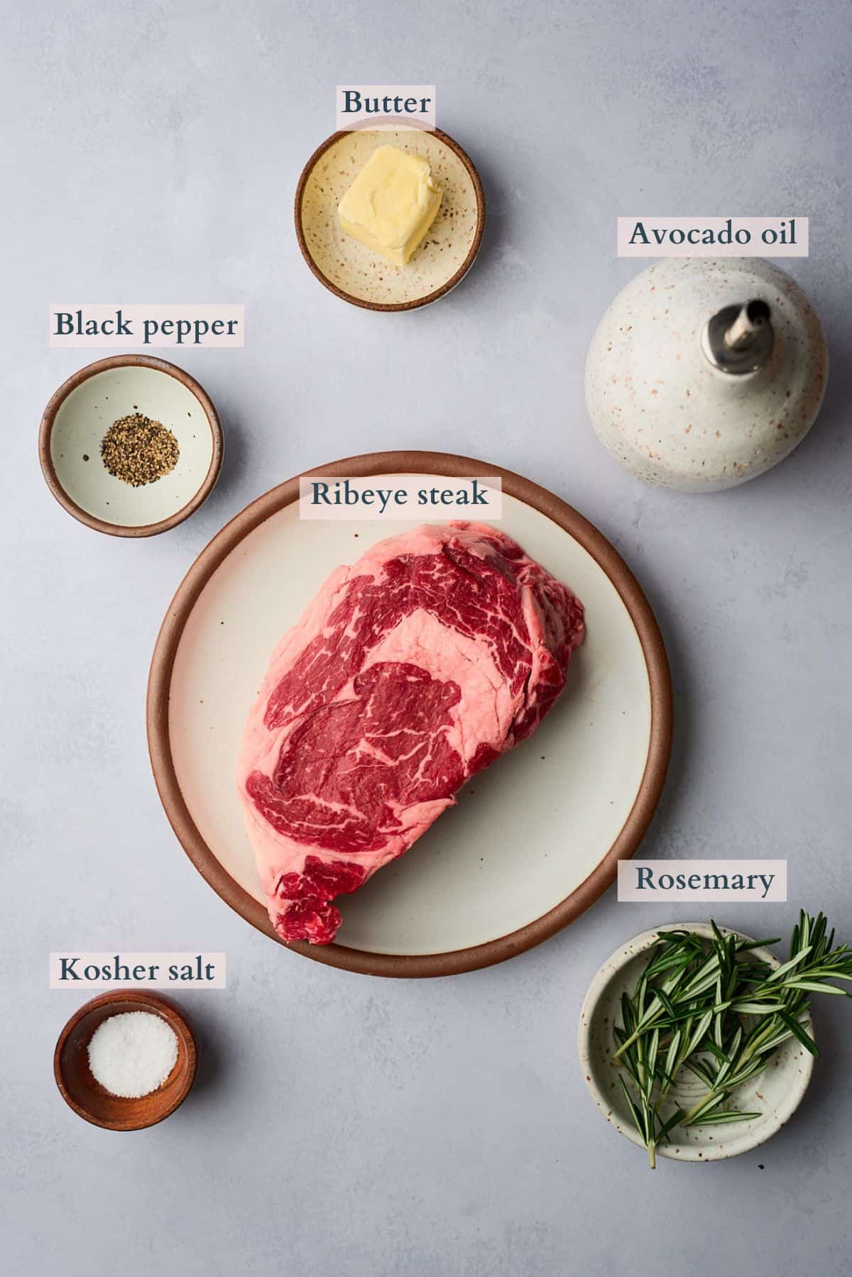 Ingredients to make a cast iron ribeye laid out on a table and labeled to denote each ingredient. 