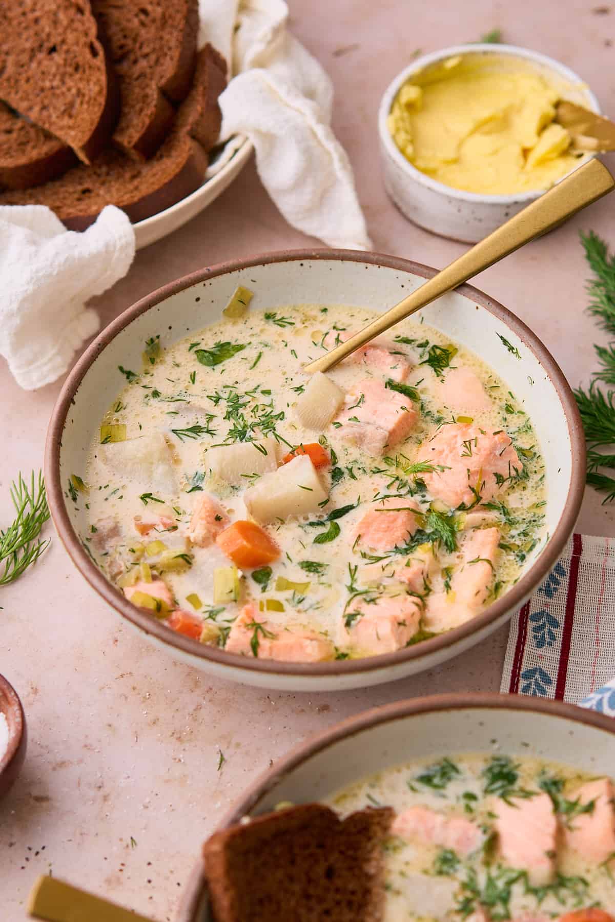 Large bowl of Finnish salmon soup with a cute patterned towel underneath, served with rye bread, butter, and fresh dill. 