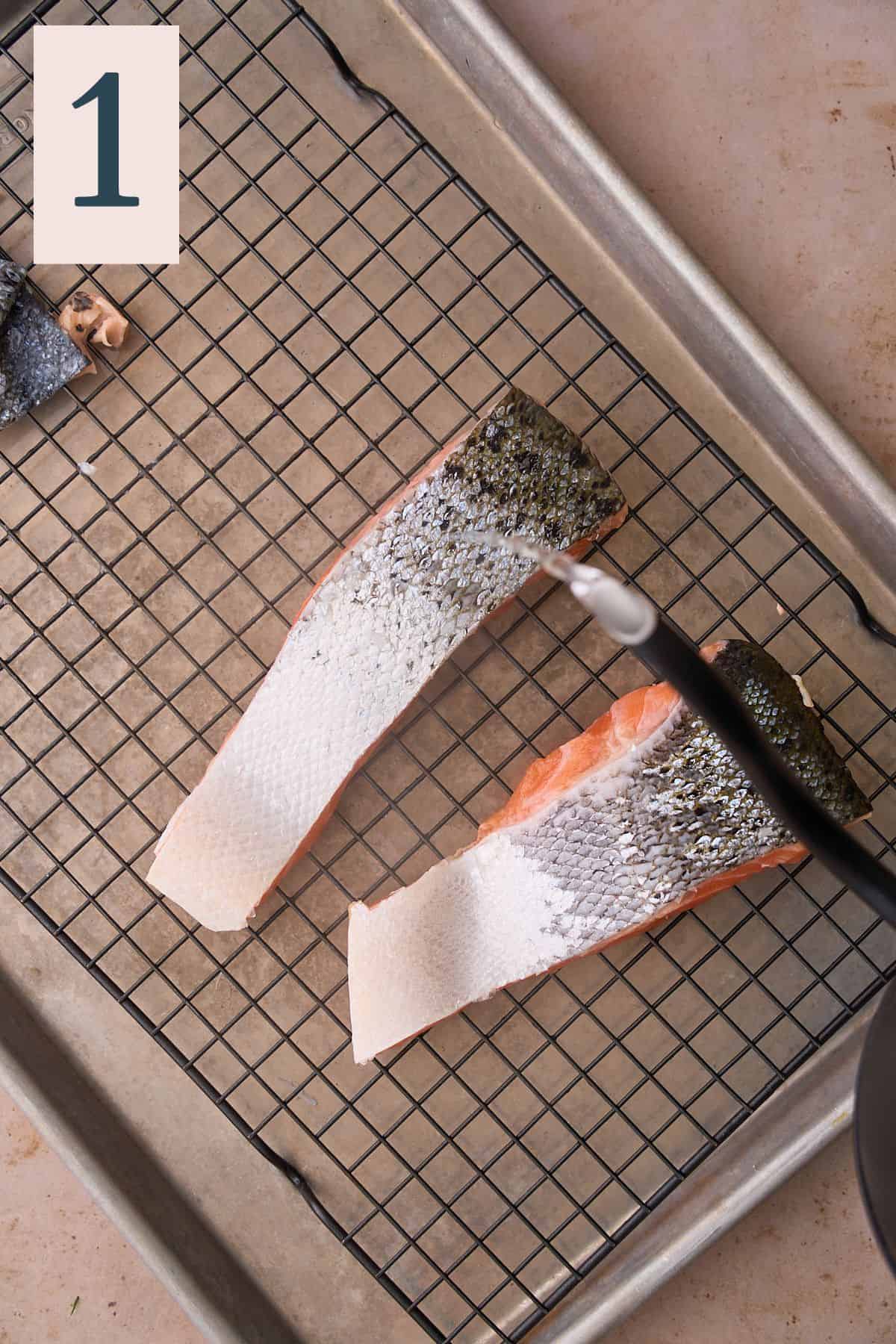 Pouring hot water over salmon skins on a baking sheet with a cooling rack.