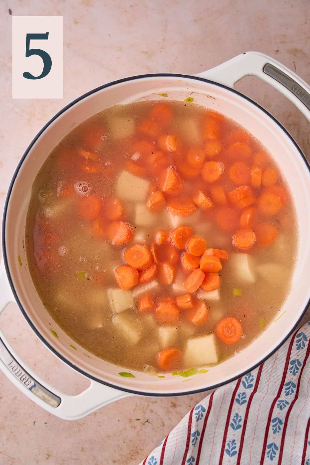 Potatoes, carrots, and fish stock added to a pot.
