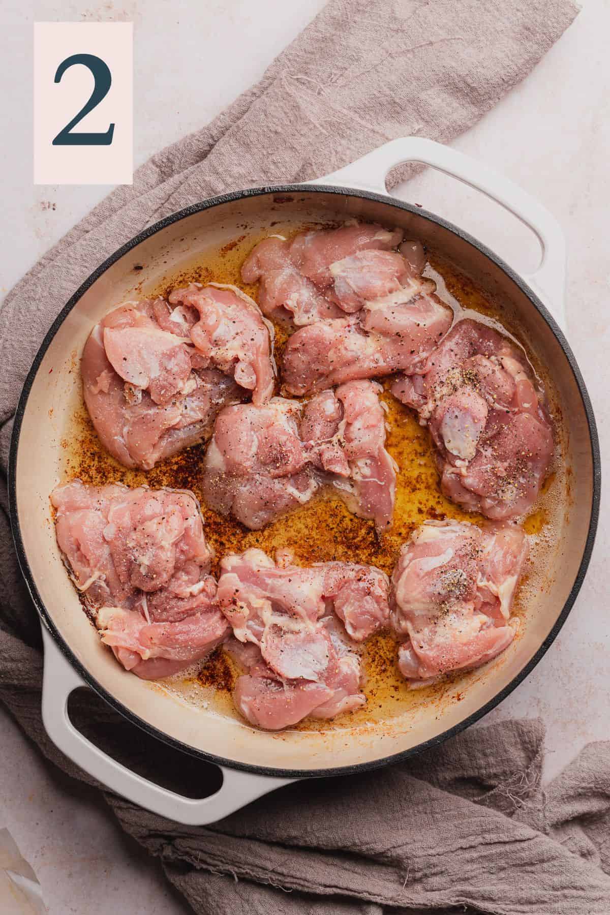 raw seasoned chicken thighs in an enameled dutch oven.