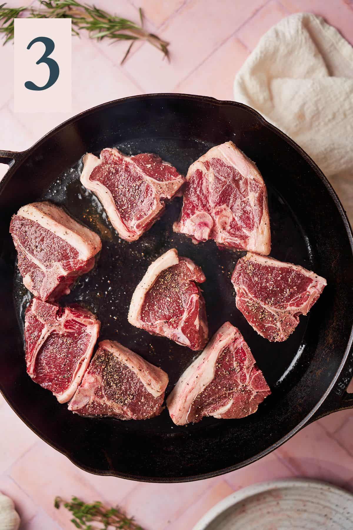 Raw lamb chops in a cast iron skillet seasoned with salt and pepper. 