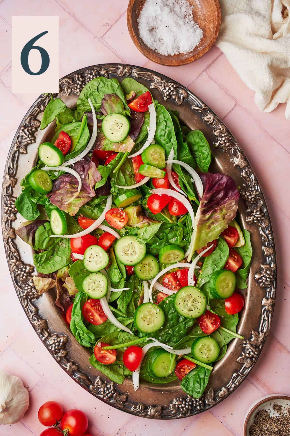 Salad on a large serving platter with onions, tomatoes, cucumbers and salt and pepper. 