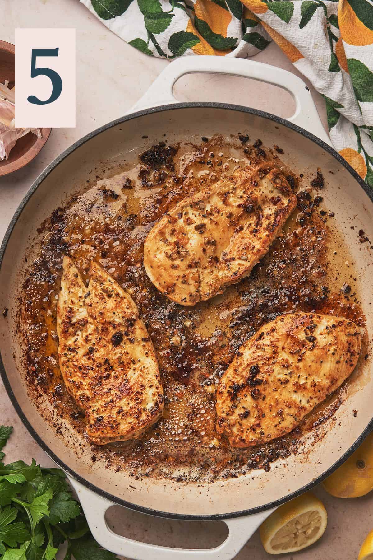 chicken breasts in a large skillet cooking in olive oil and butter.