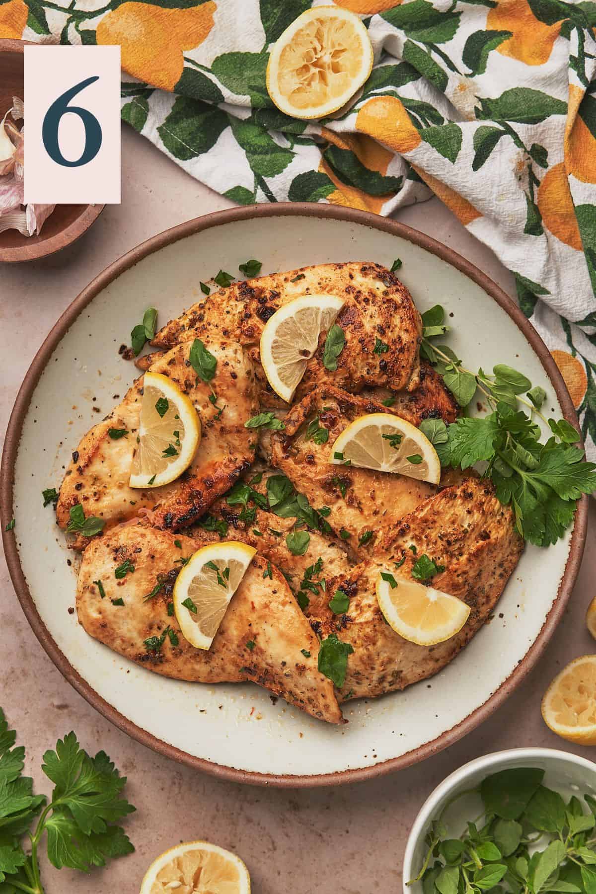 lemon herb chicken on a plate with fresh parsley, oregano, and lemon slices.