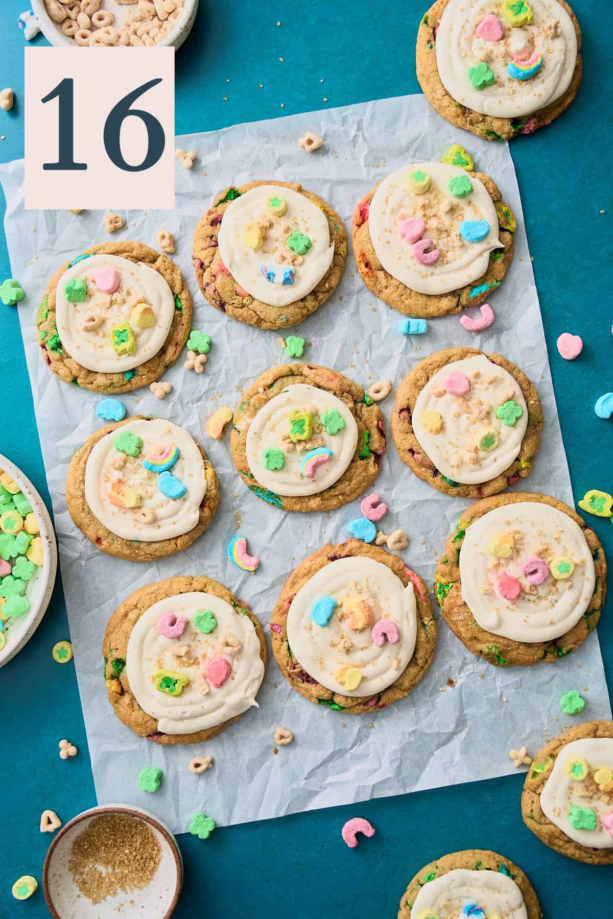 Lucky Charms cookies with marshmallow frosting and topped with more cereal on a parchment lined baking sheet. 