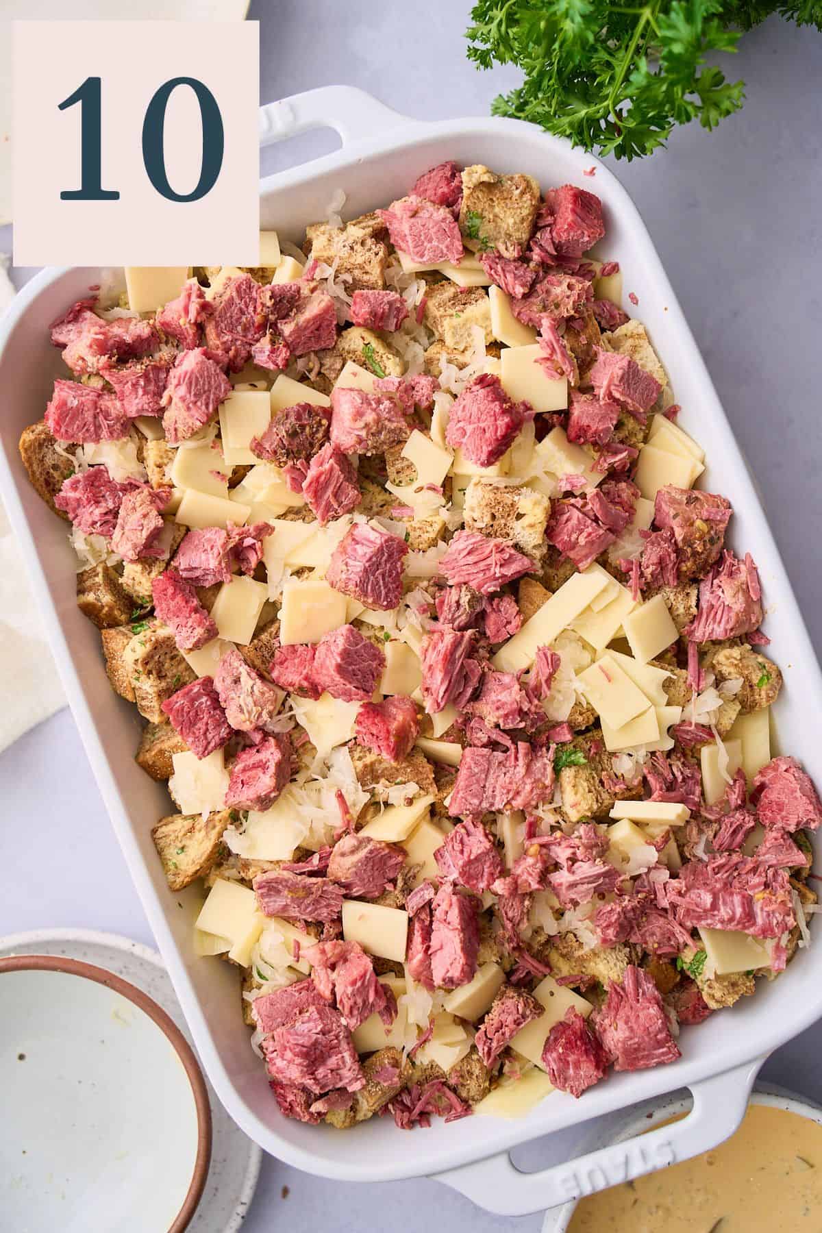 Adding the last layer of corned beef on top of the cheese and sauerkraut in a casserole dish. 