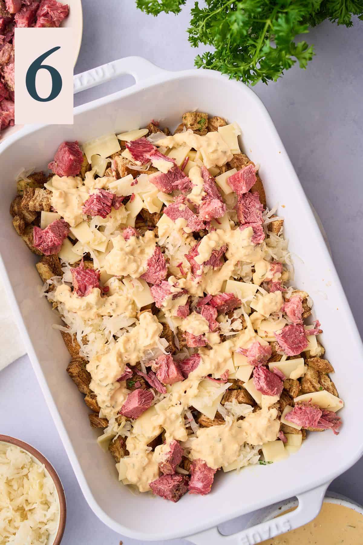 Layering on swiss cheese, corned beef, and sauerkraut on top of bread pieces in a casserole dish. 