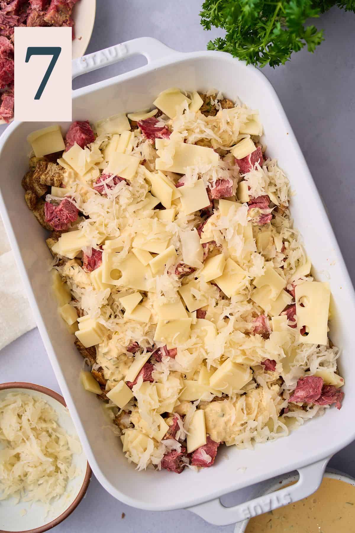 Layering more corned beef, sauerkraut, and Swiss cheese in a casserole dish. 