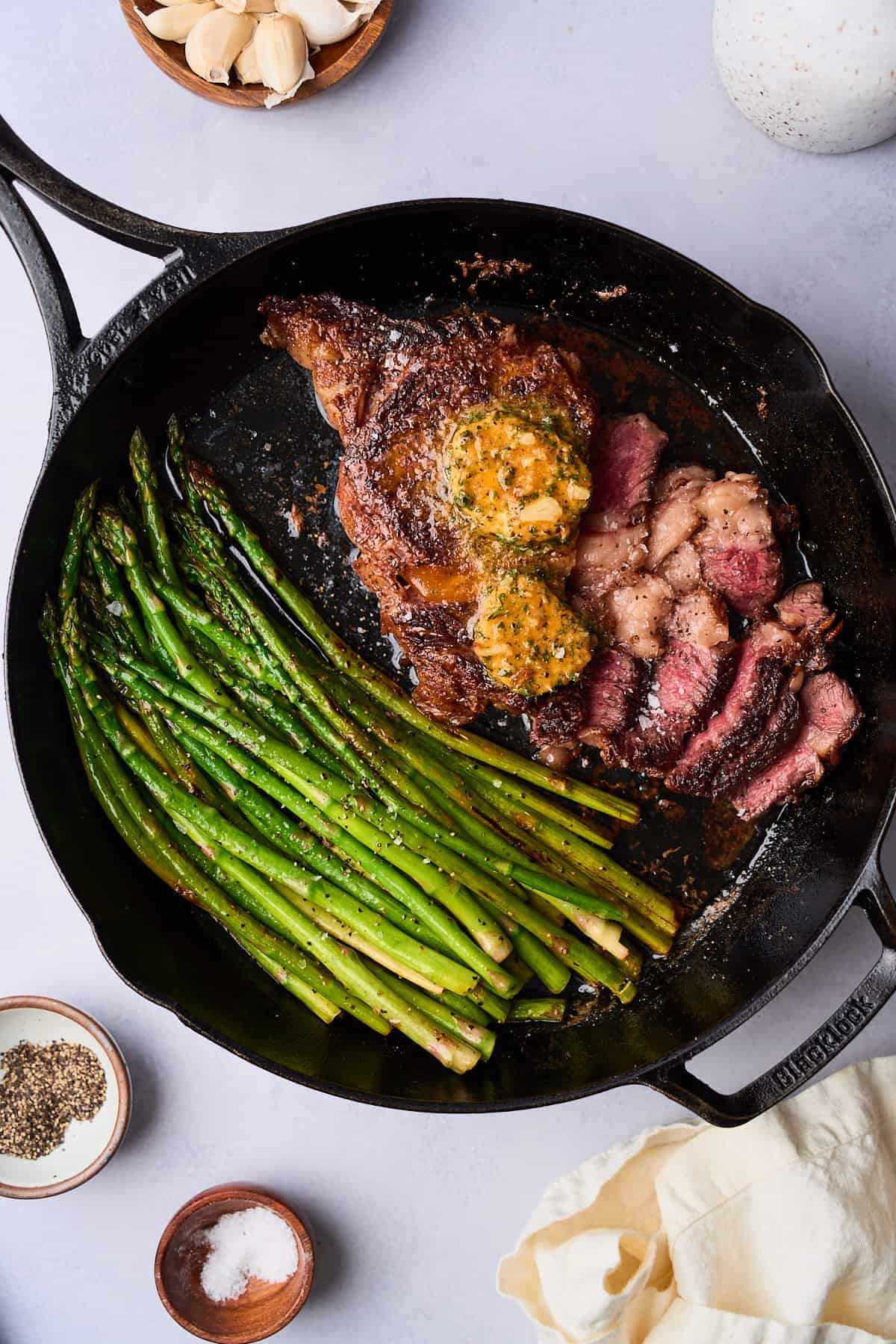 Ribeye steak and asparagus cooked in a cast iron skillet, topped with melting compound butter, and cut into to reveal the center cooked a perfect medium rare.