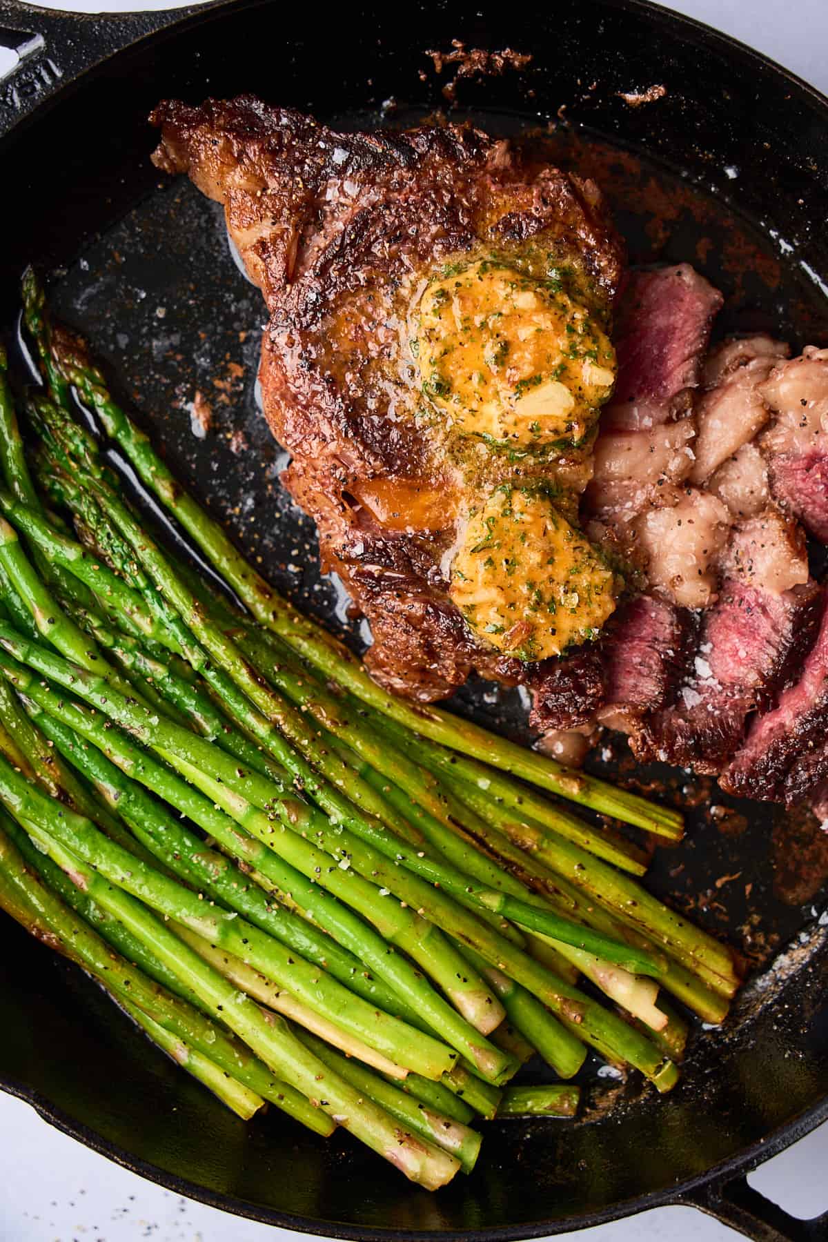 Close up shot of a cast iron ribeye steak with asparagus, with the steak cut into to reveal the delicious medium rare cook on the steak. 