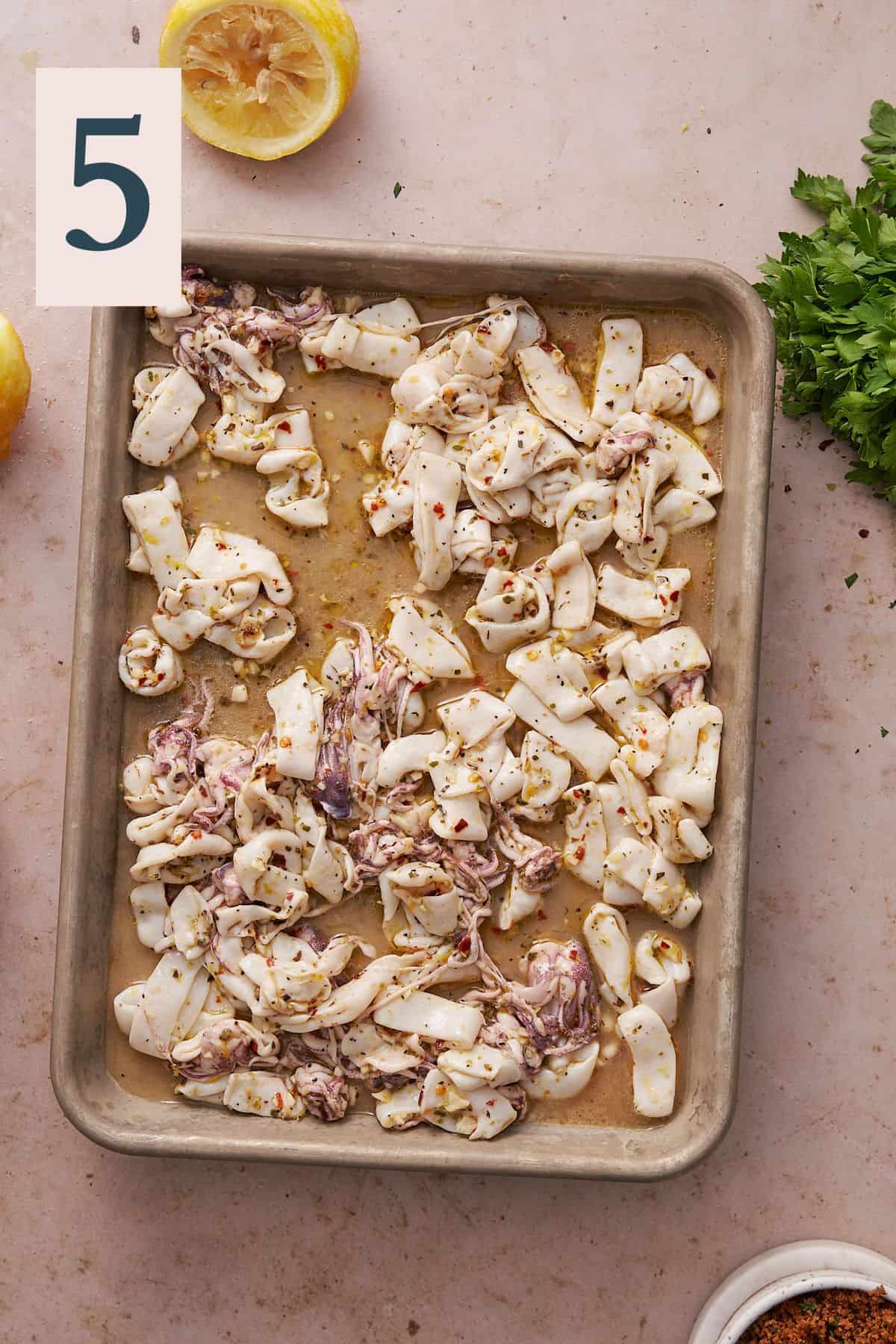 calamari on a baking sheet with seasonings, olive oil, and lemon juice.