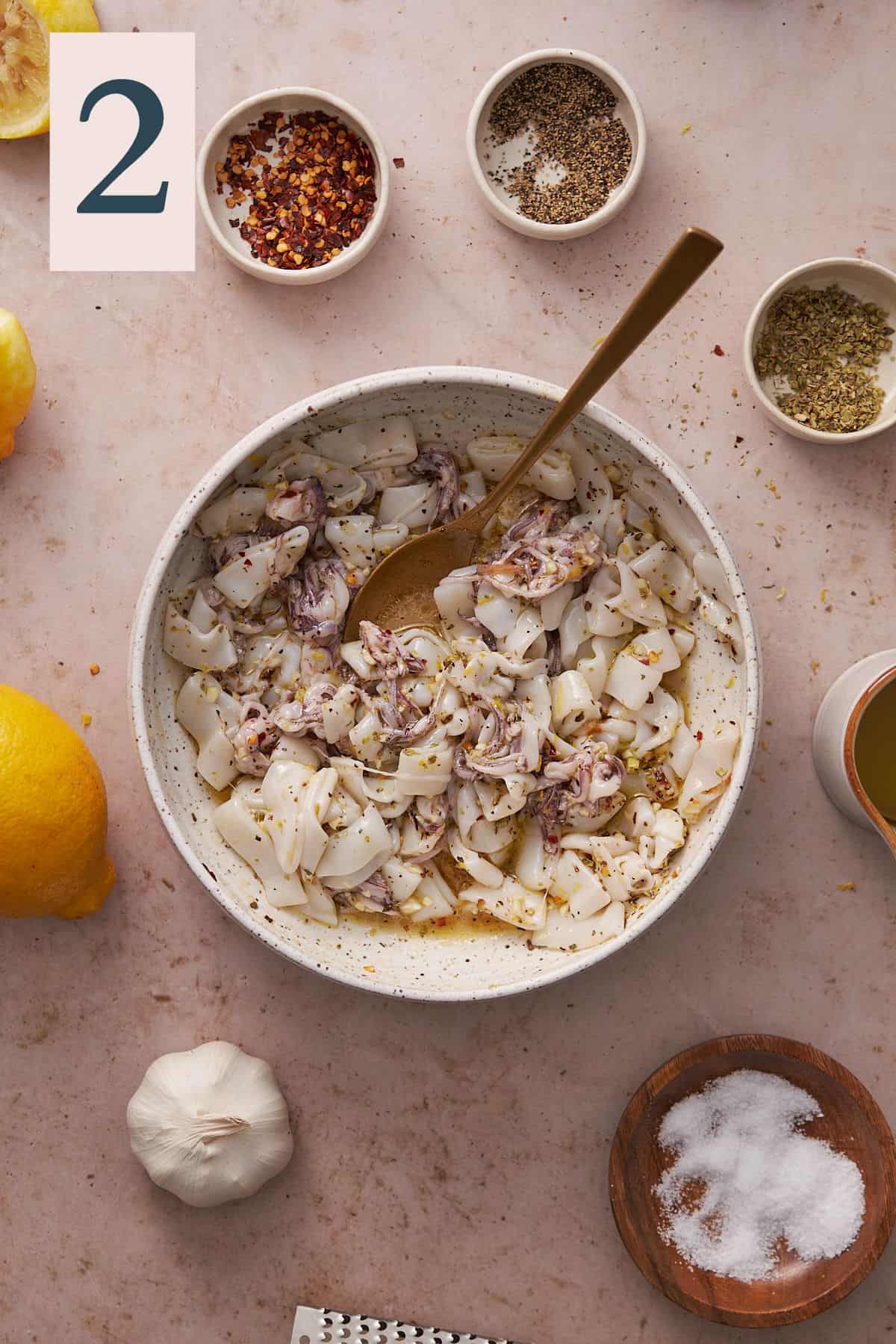 calamari in a bowl marinating with seasonings, olive oil and lemon juice.