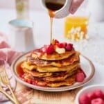 Beautiful stack of sweet cream pancakes being drizzled with maple syrup and topped with berries.