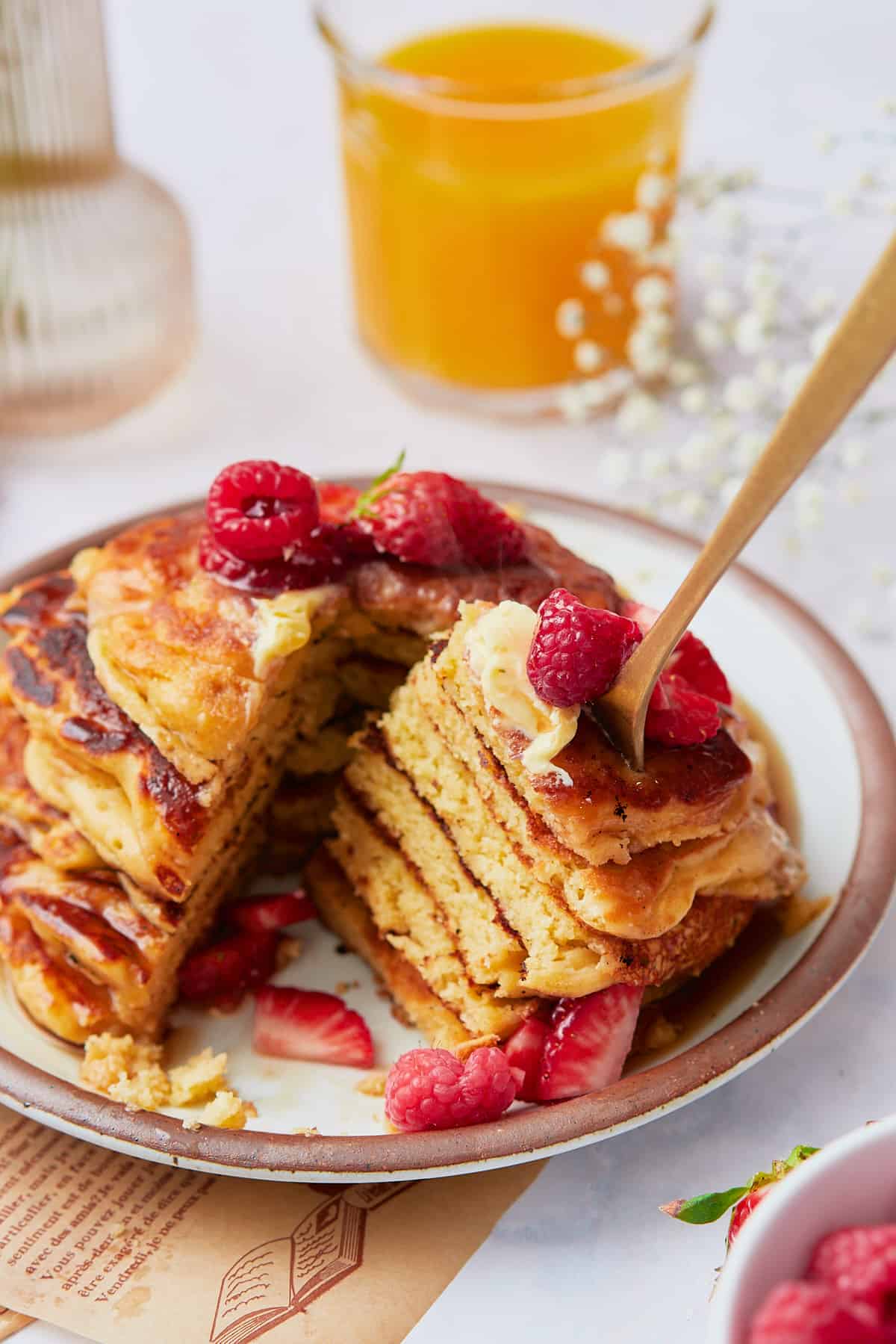 Stack of pancakes topped with butter and fresh berries, with a big bite taken out with a fork.