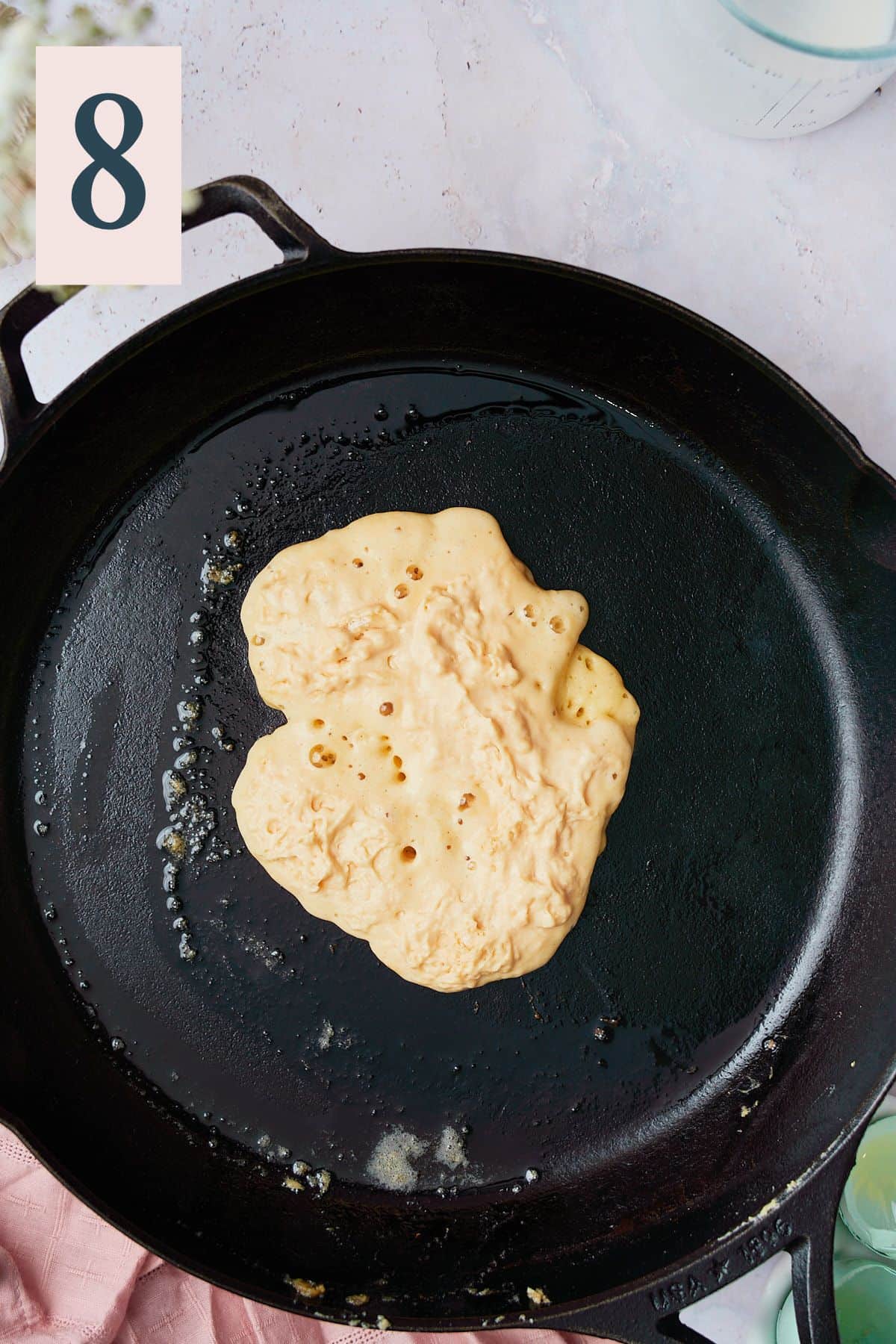 Pancake in a large skillet beginning to get bubbles on the top. 