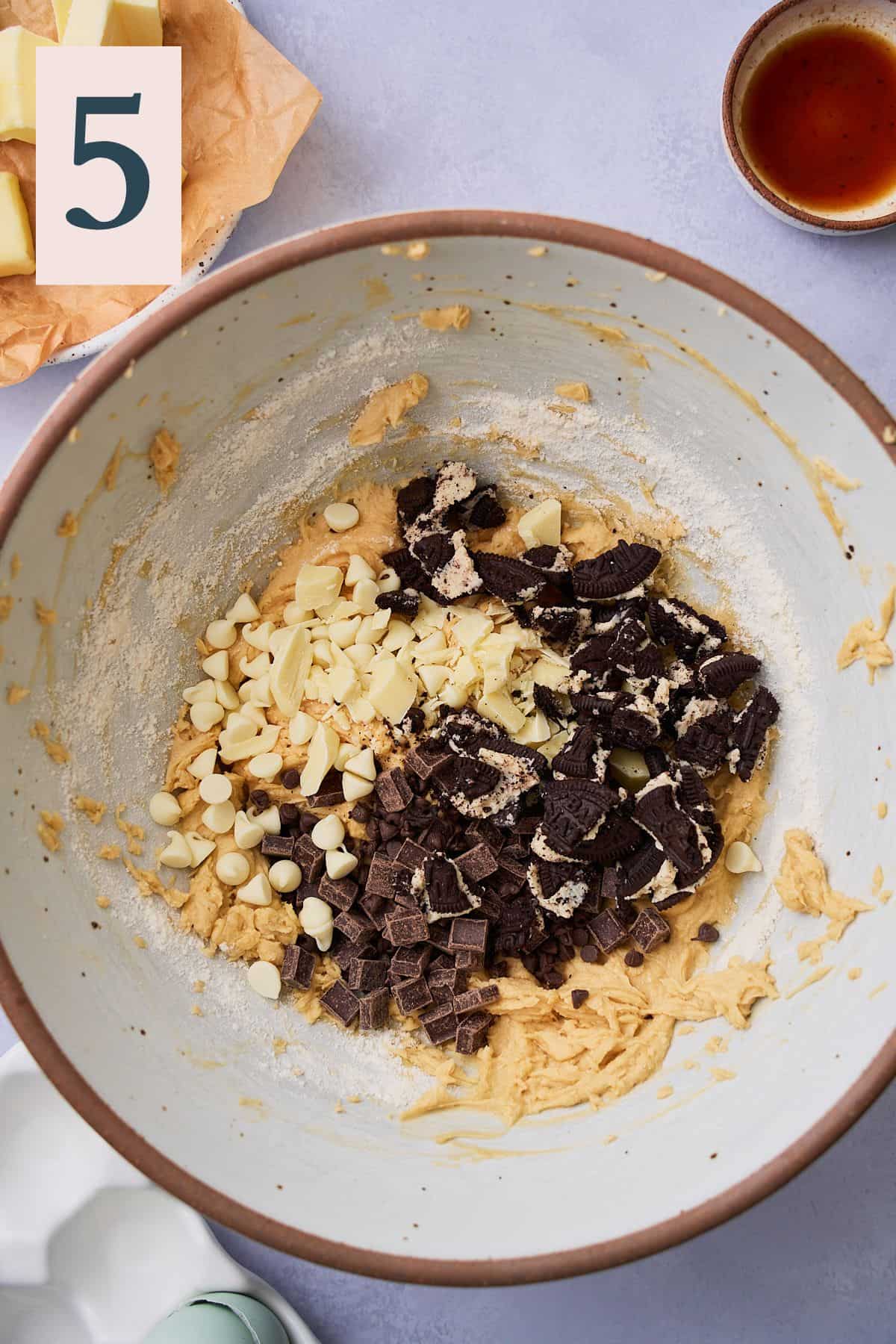 Cookie dough mixed together in a bowl with white, dark, semi-swet chocolate, and cookie pieces added. 