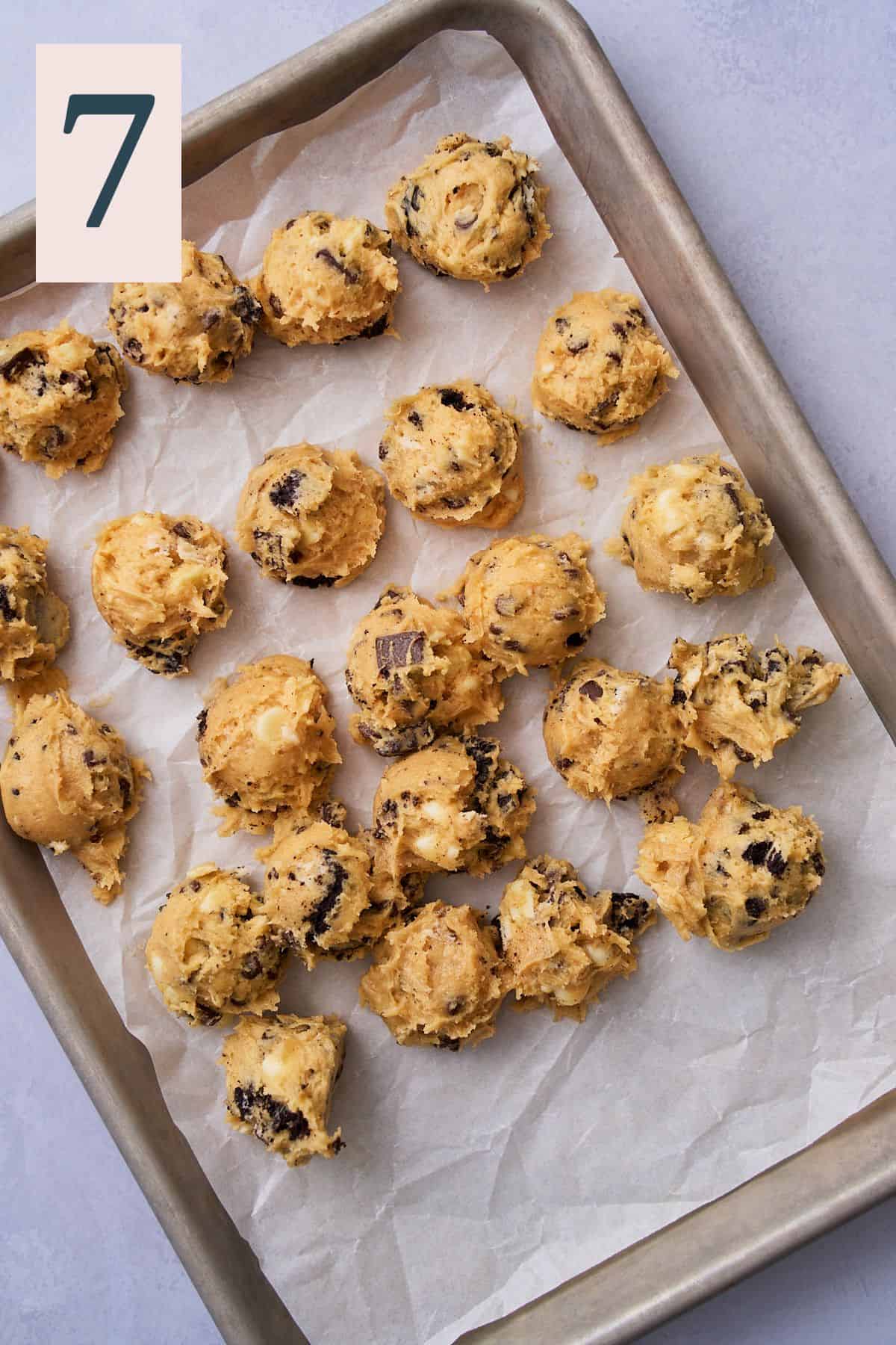 Small pieces of chocoalte chip cookie dough on a parchment lined baking sheet.