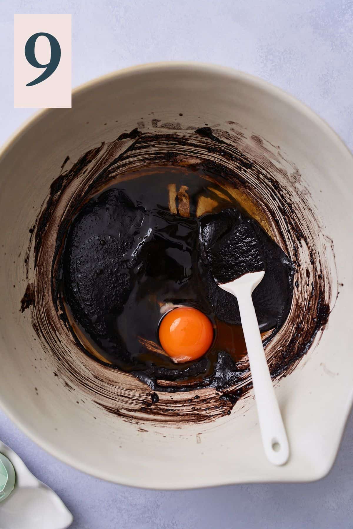 Dark cocoa, butter, and sugar mixture in a bowl with vanilla extract and an egg added. 