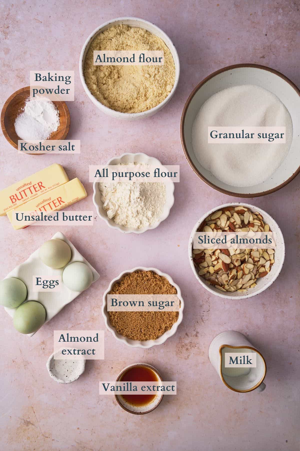 Ingredients to make Swedish almond cake laid out on a table in small bowls and labeled to denote each ingredient.