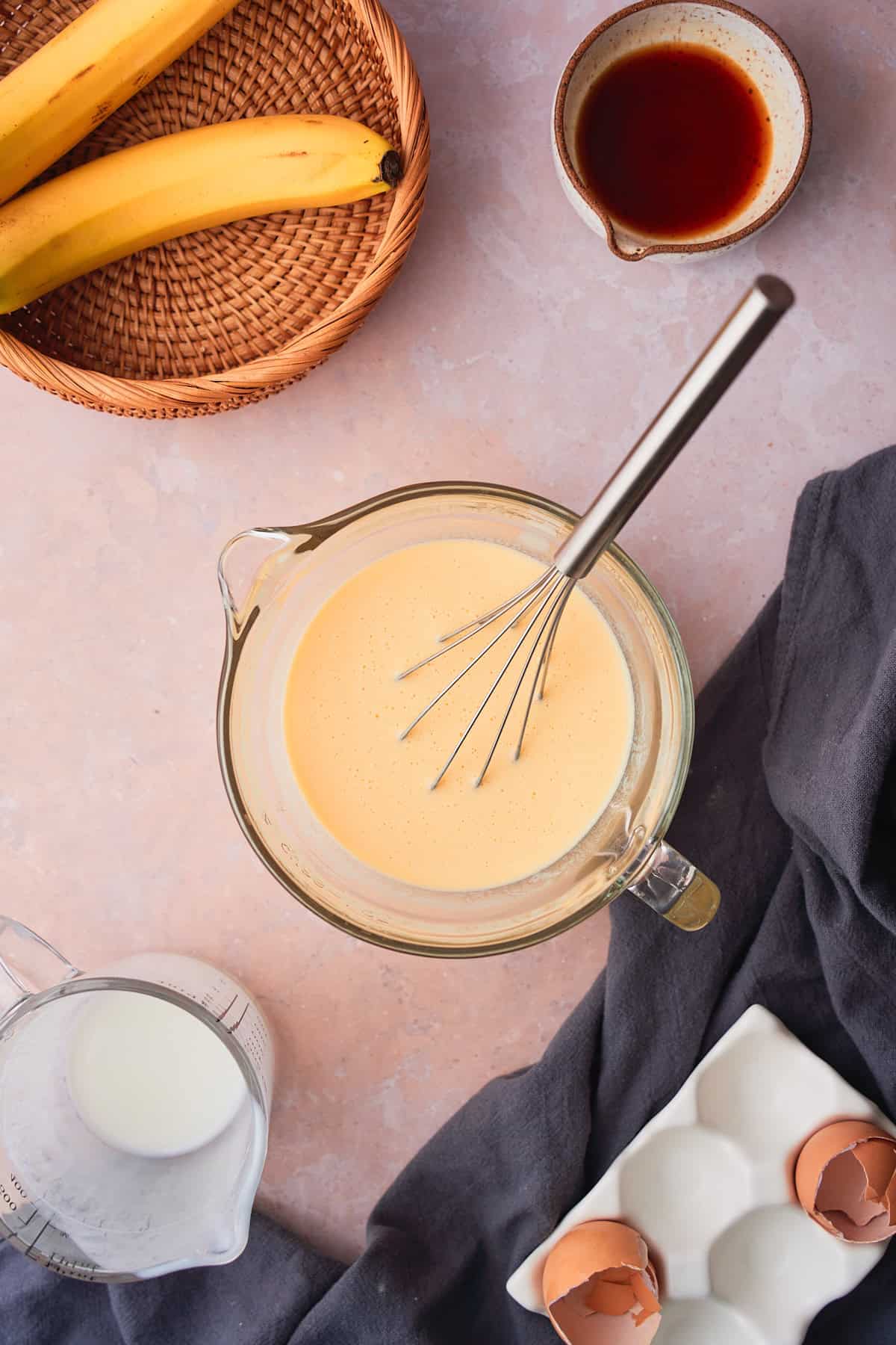 Buttermilk, vanilla, and eggs whisked together in a bowl with a few of the ingredients surrounding it. 
