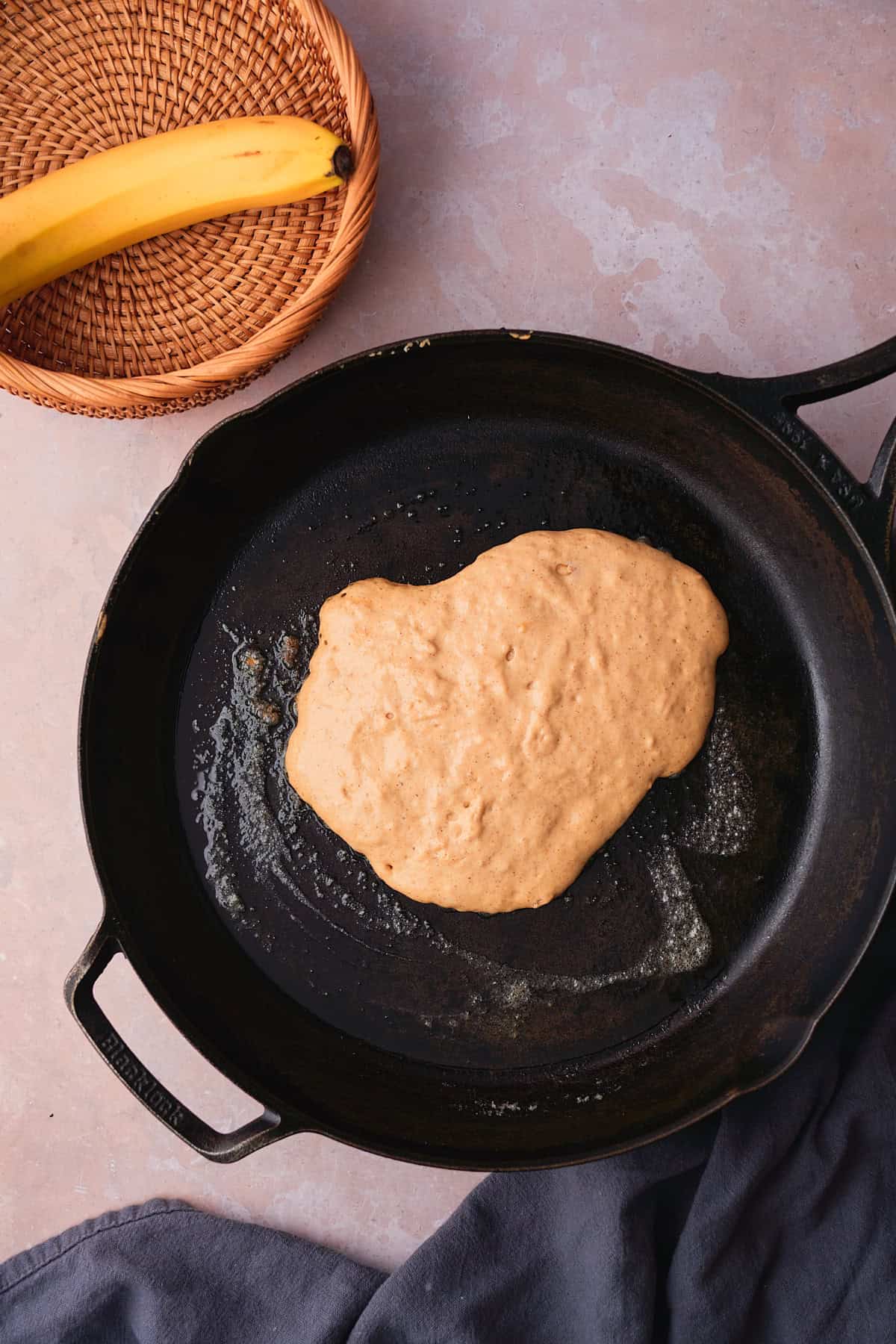Raw pancake batter in a cast iron skillet with butter, with bubbles forming on the top of the pancake letting you know it's ready to flip. 