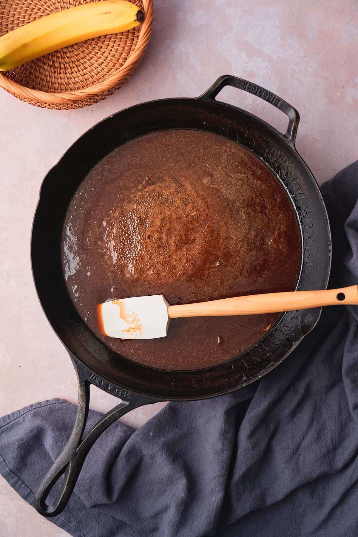 Brown sugar, rum, butter, cinnamon and salt gently forming a caramel like sauce in a skillet with a rubber spatula in it. 