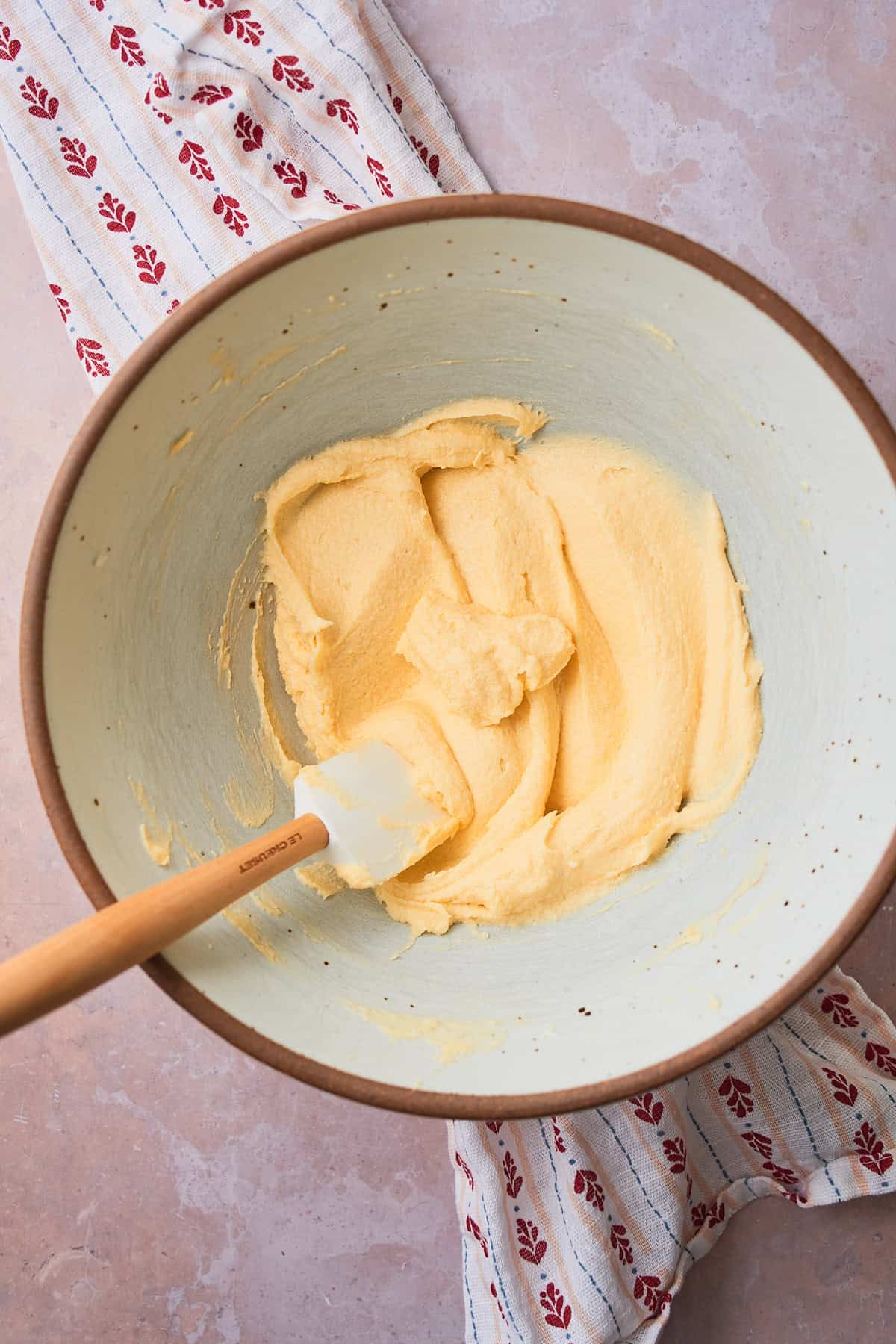 Smooth mixture of butter, sugar, eggs, cream cheese and extracts creamed together in a large bowl to make smooth mixture with a rubber spatula in the bowl. 