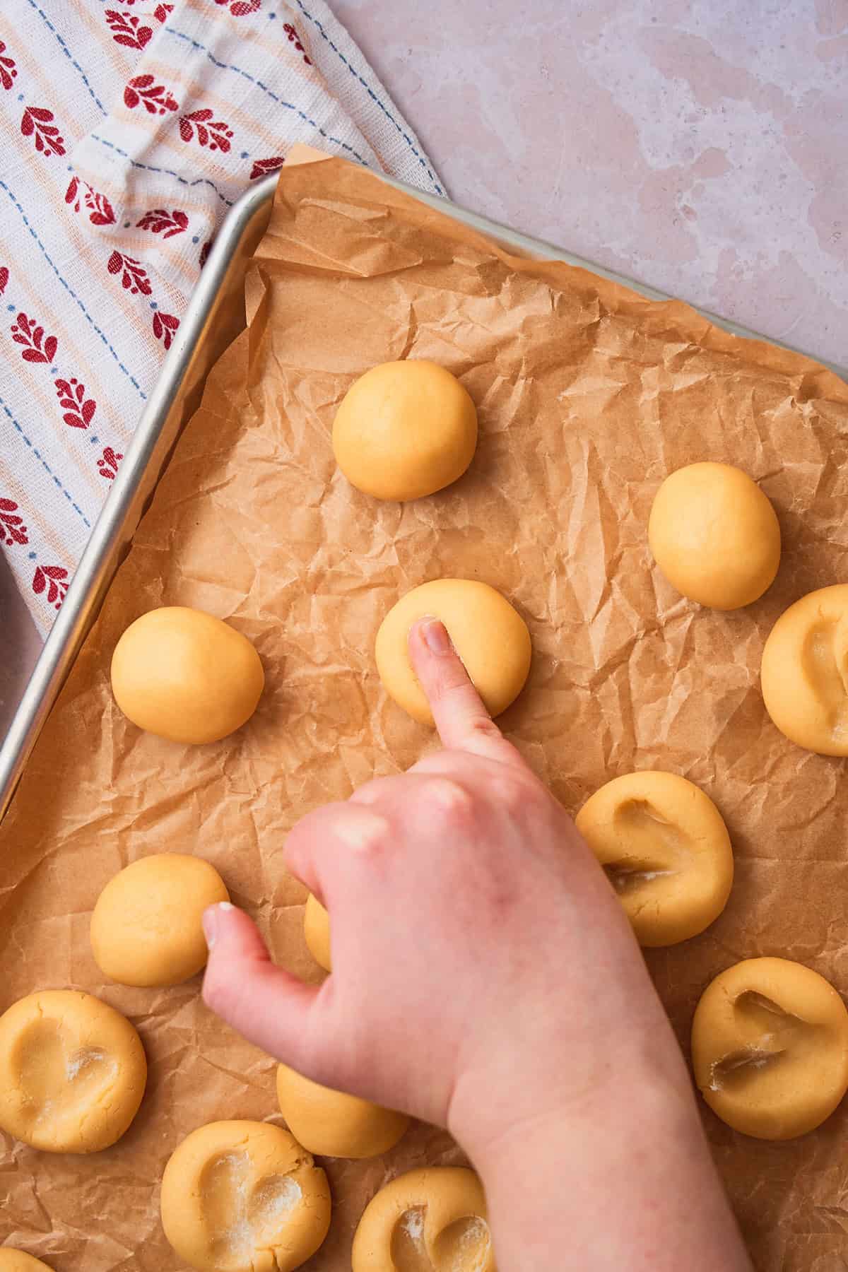 Pinky finger pressing into a ball of cookie dough to begin making a heart shape. 