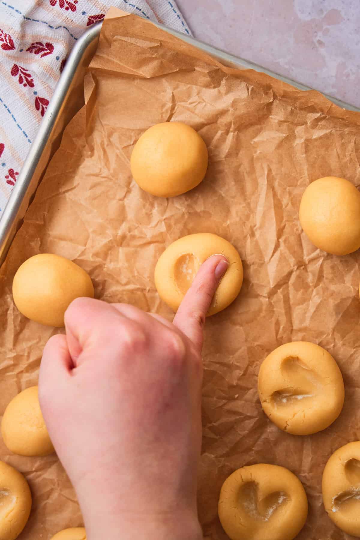 Pinky finger making a second indent into a ball of cookie dough making a heart shape.